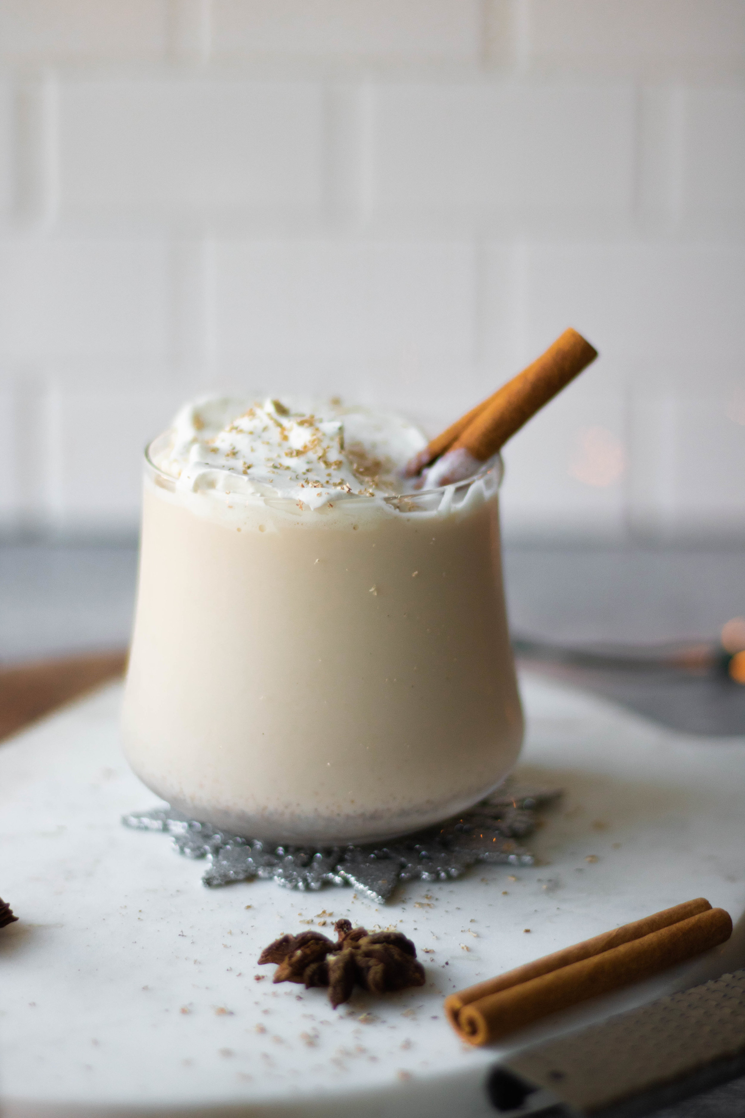 Glass of hard eggnog topped with whipped cream and a cinnamon stick. 