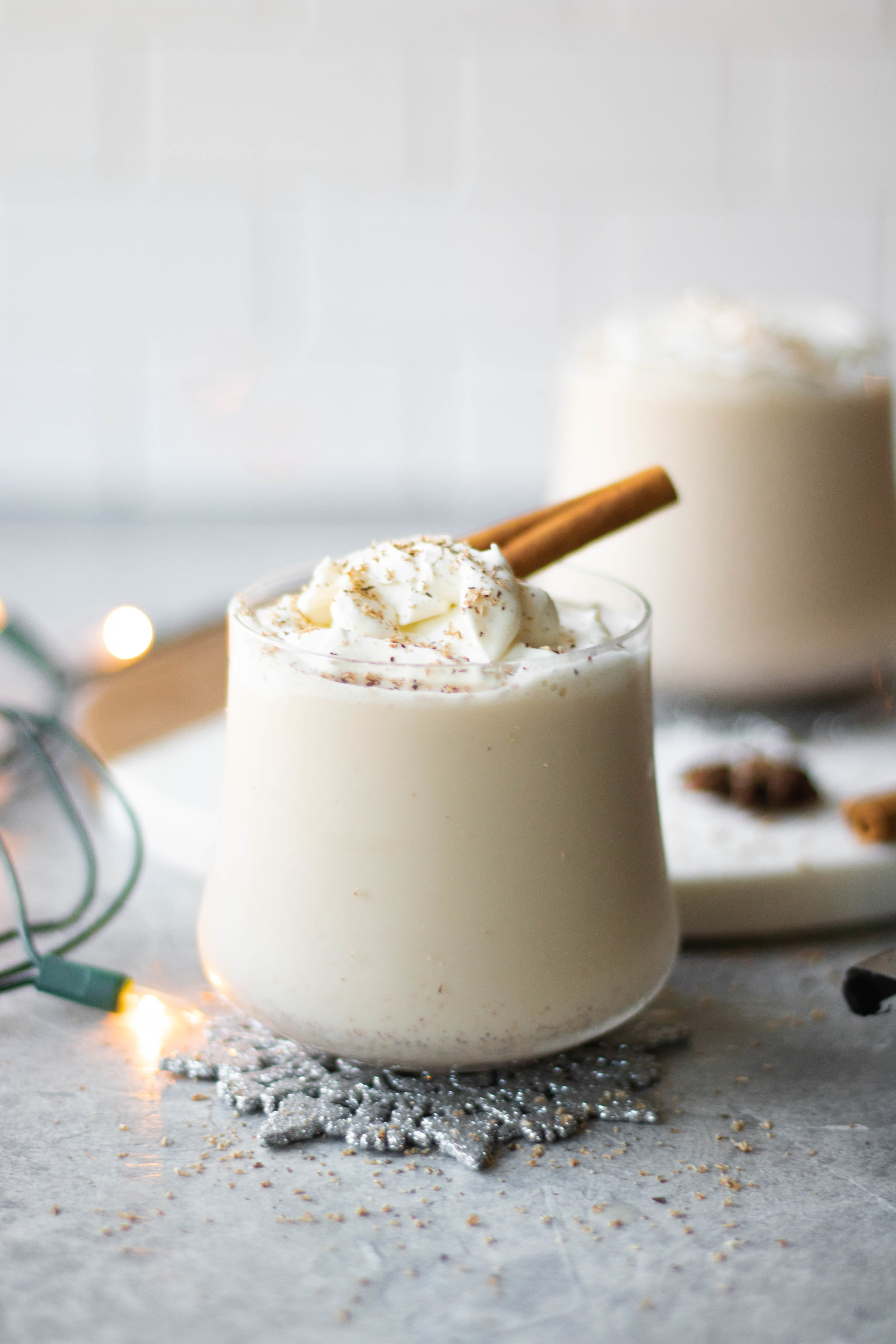 Glass of boozy eggnog topped with whipped cream and a cinnamon stick. 