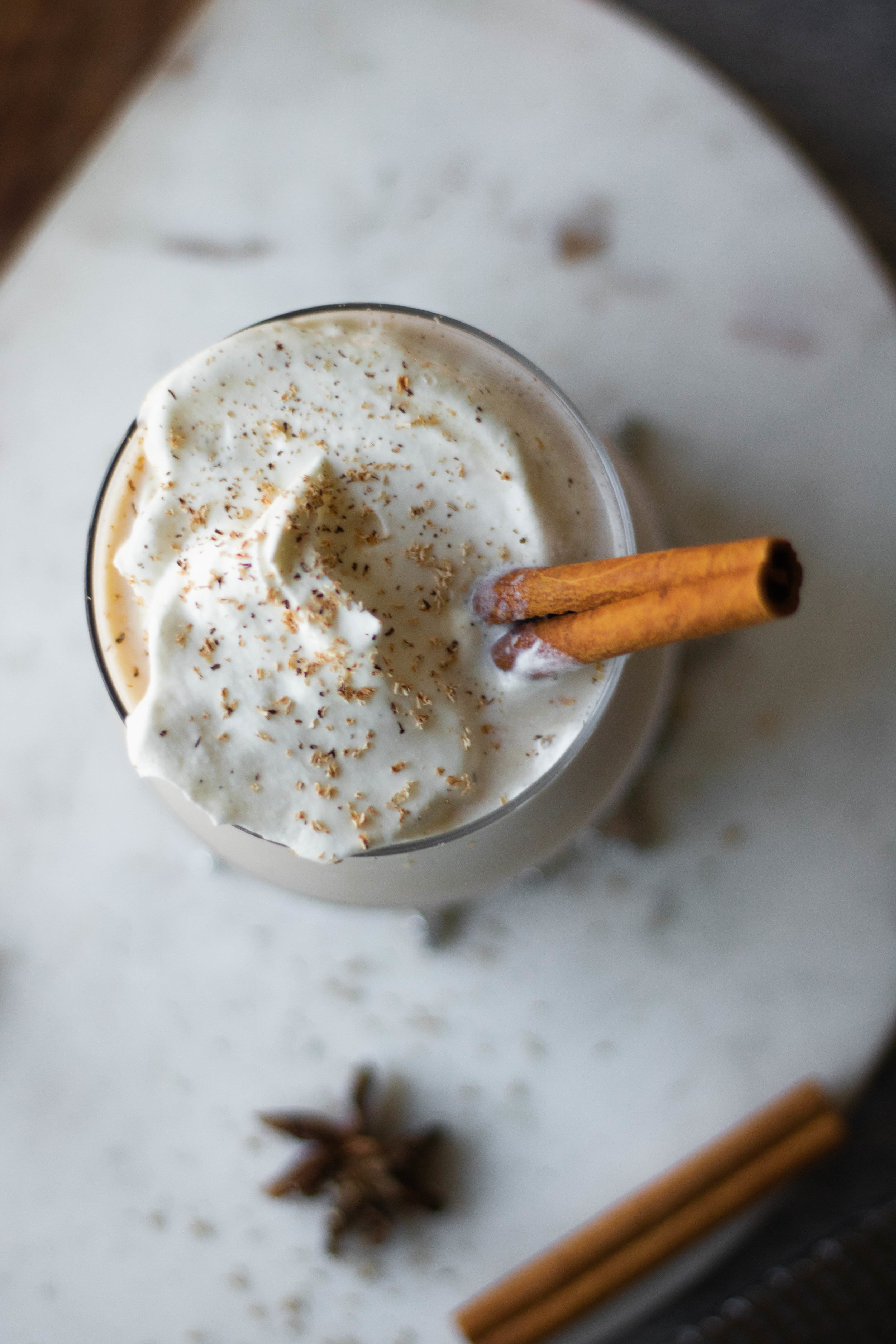 Glass of rum and brandy eggnog topped with whipped cream and a cinnamon stick. 