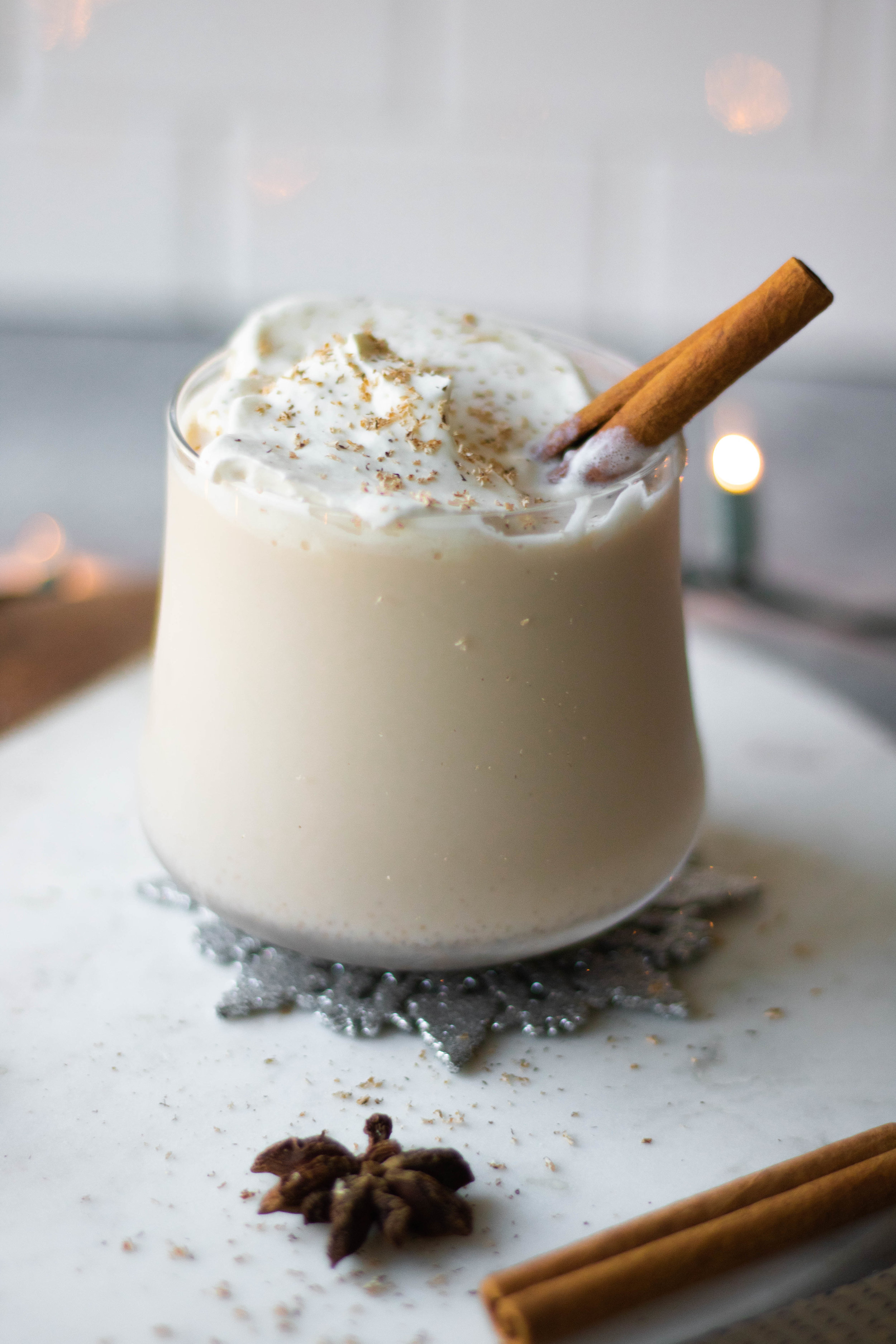 Glass of boozy eggnog topped with whipped cream and a cinnamon stick. 