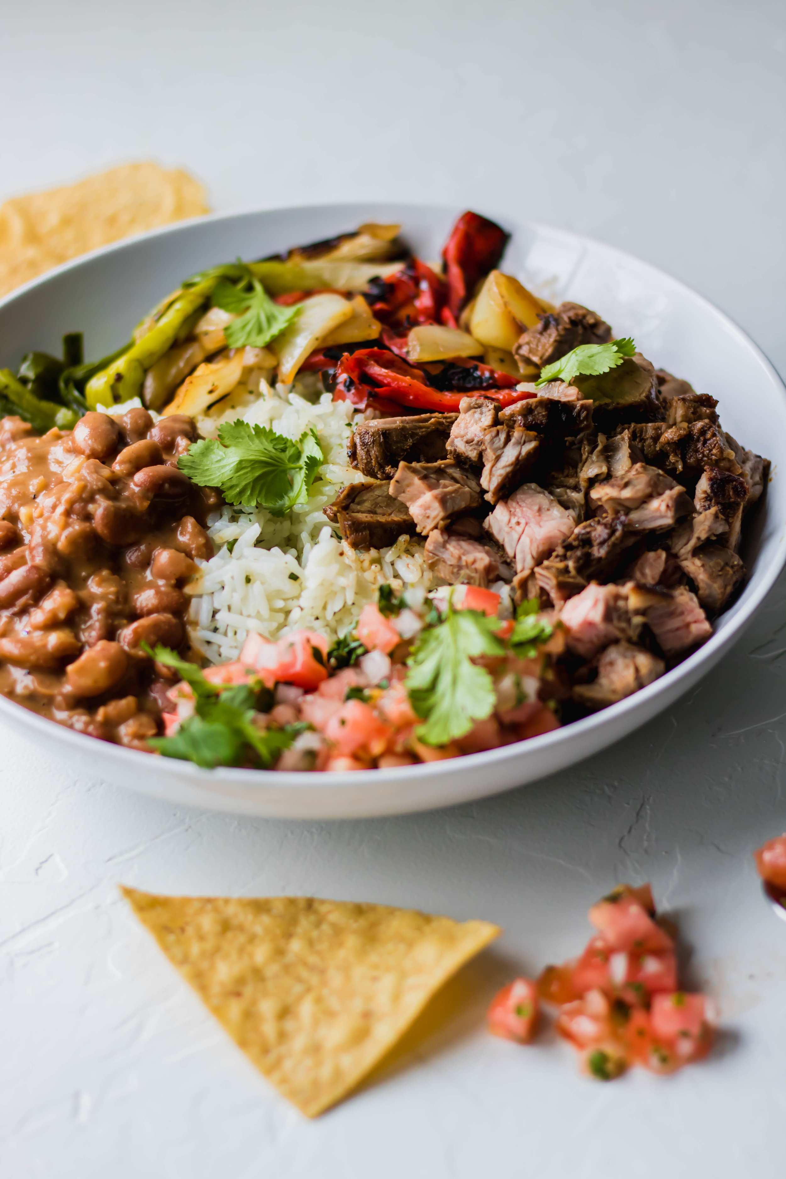 A carne asada bowl topped with sauteed veggies and fresh cilantro 