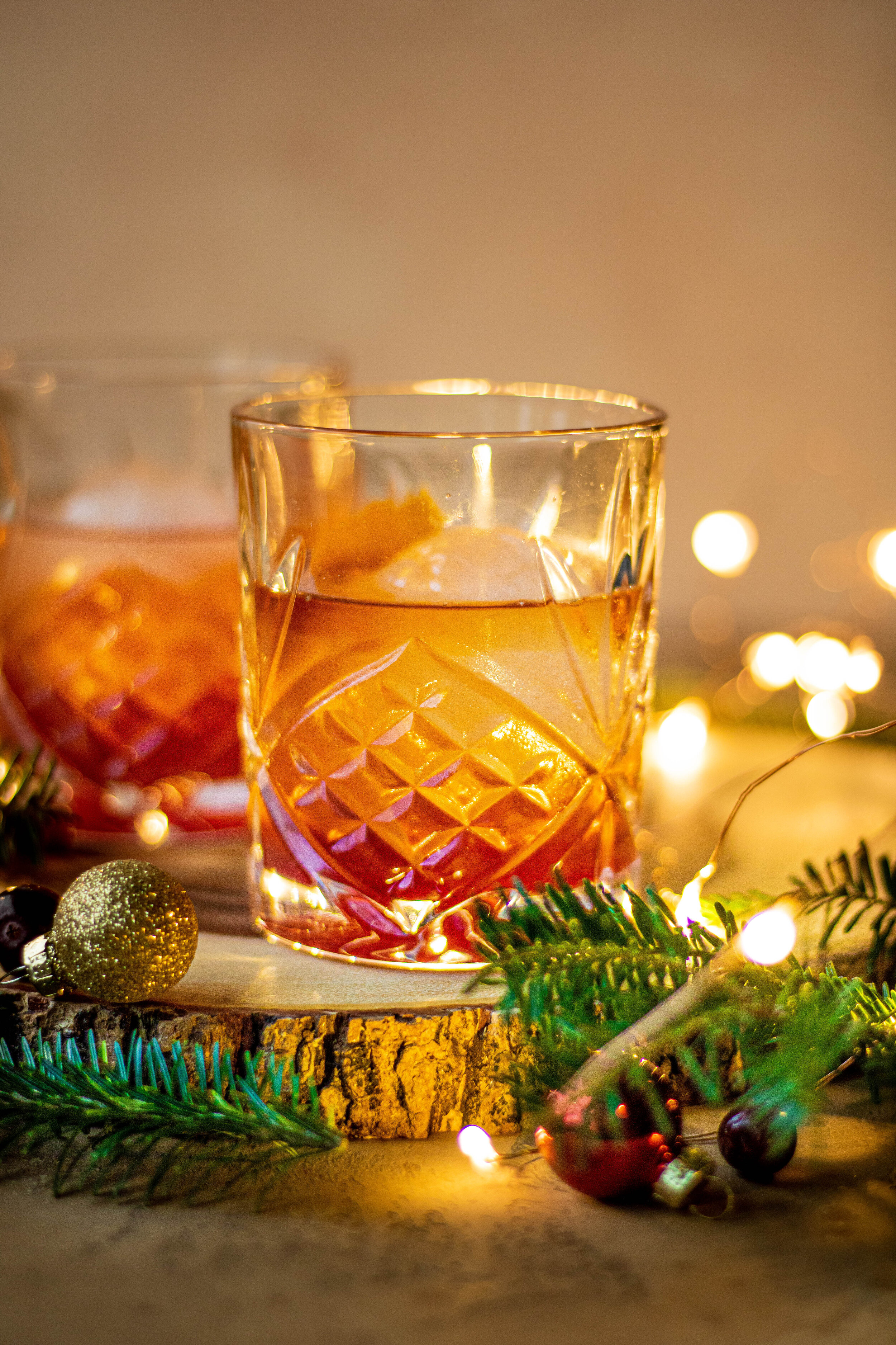 two cranberry old fashioned cocktails with twinkle lights