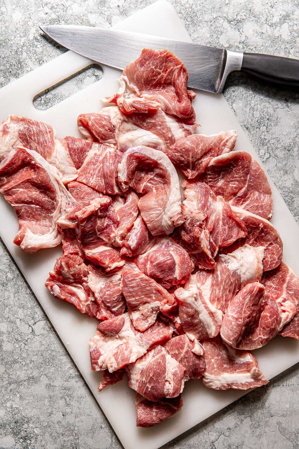 thinly sliced pork on a cutting board with a knife