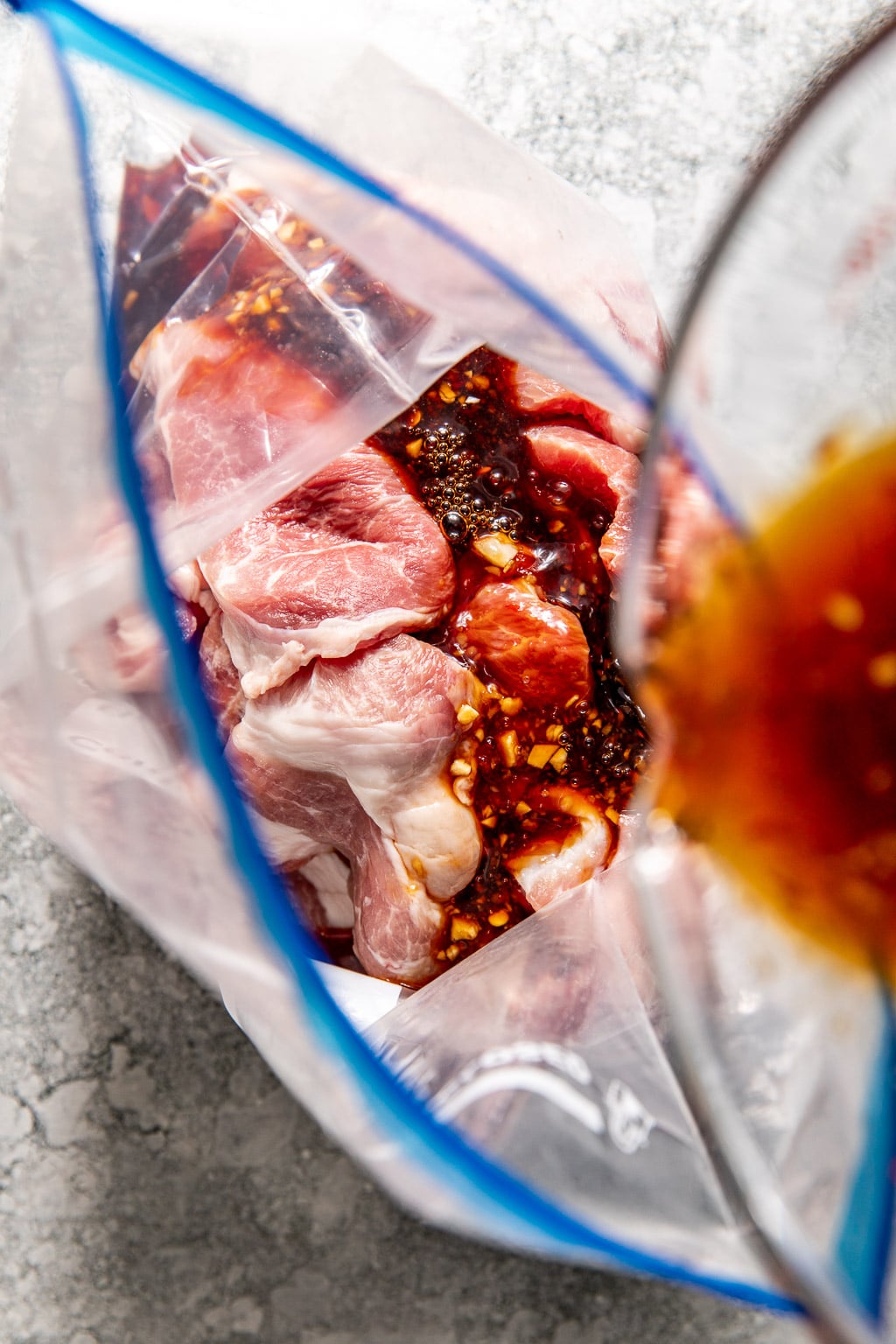 marinade being poured into a ziplock bag over the pork