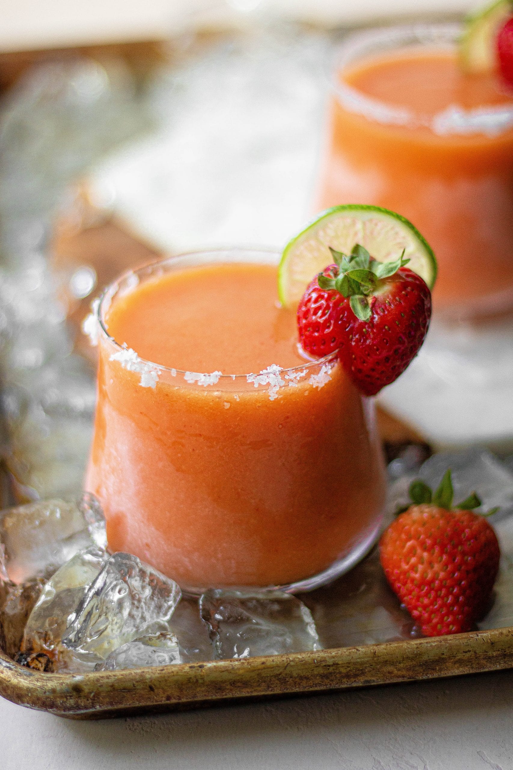 a strawberry mango margarita rimmed with salt and garnished with lime and strawberry