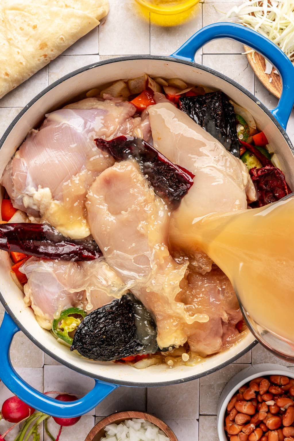 Adding all of the ingredients for pozole to a large pot 