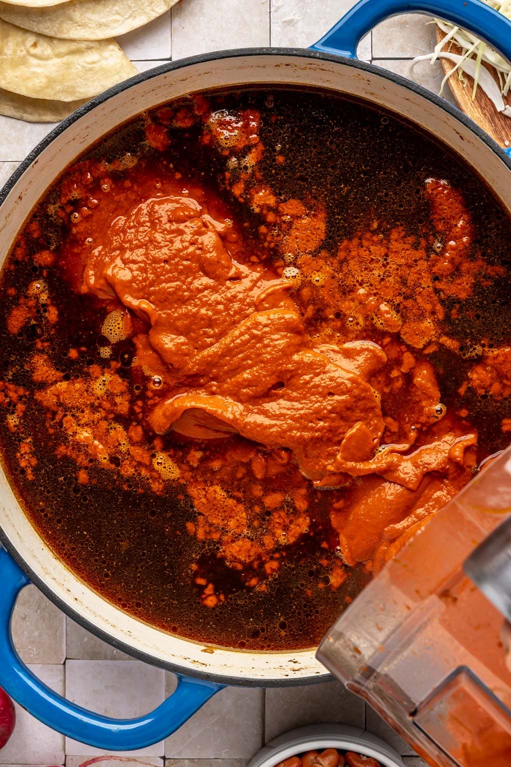 Returning the blended vegetables to a pot of pozole 
