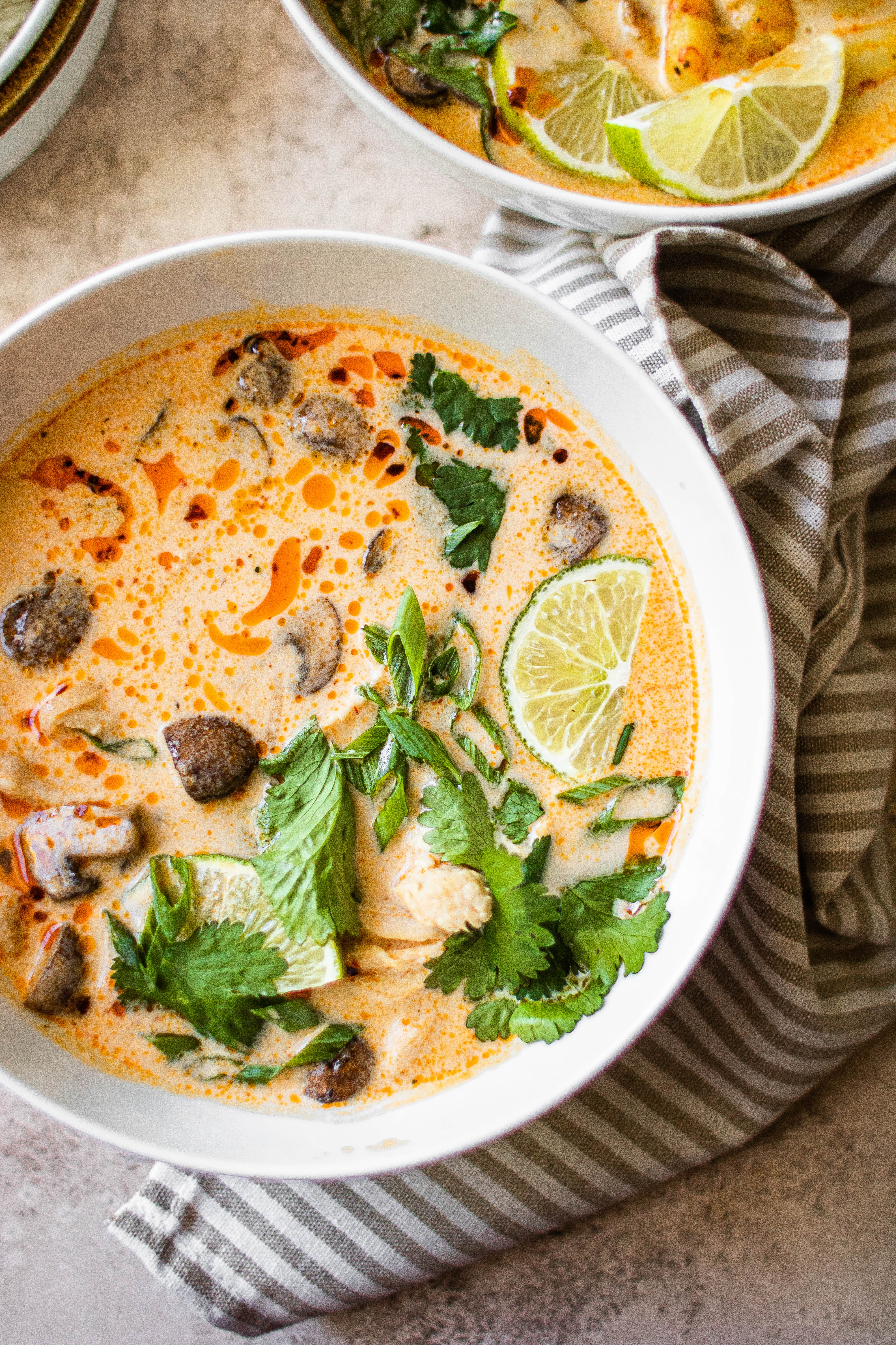 A bowl of Tom Kha Gai soup garnished with cilantro and lime 
