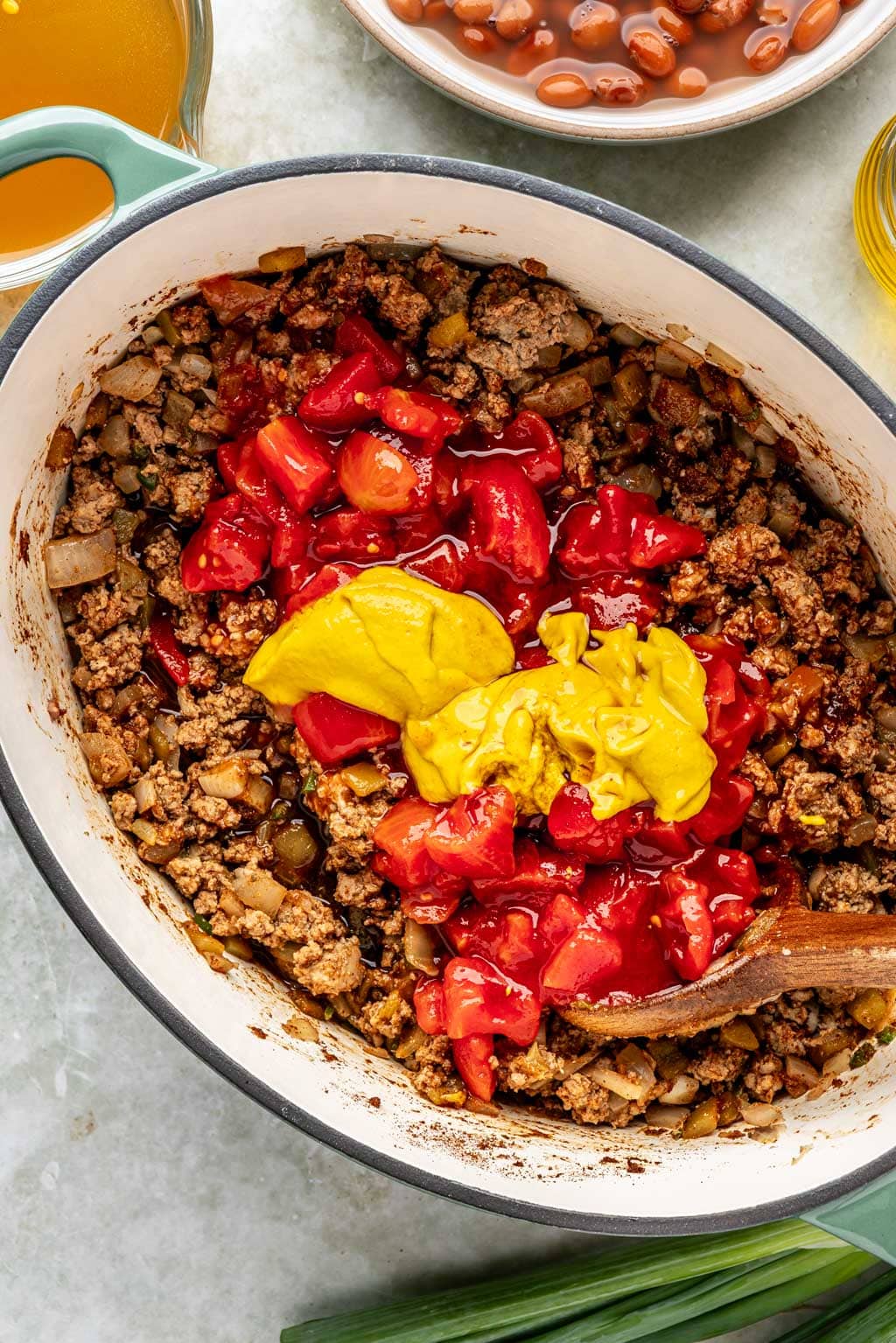 tomatoes and mustard being added to the chili