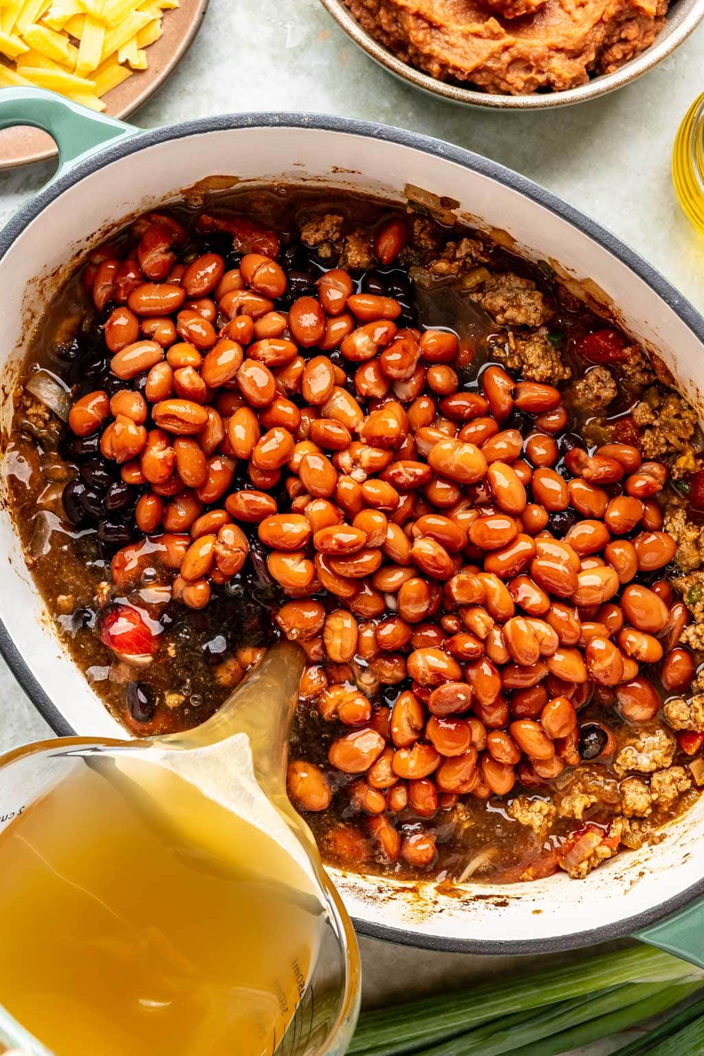 beans and broth being added to the chili