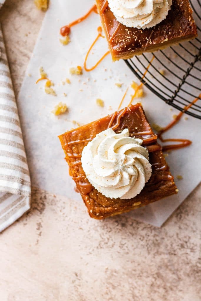 A pumpkin pie bar topped with maple whipped cream and salted caramel sauce