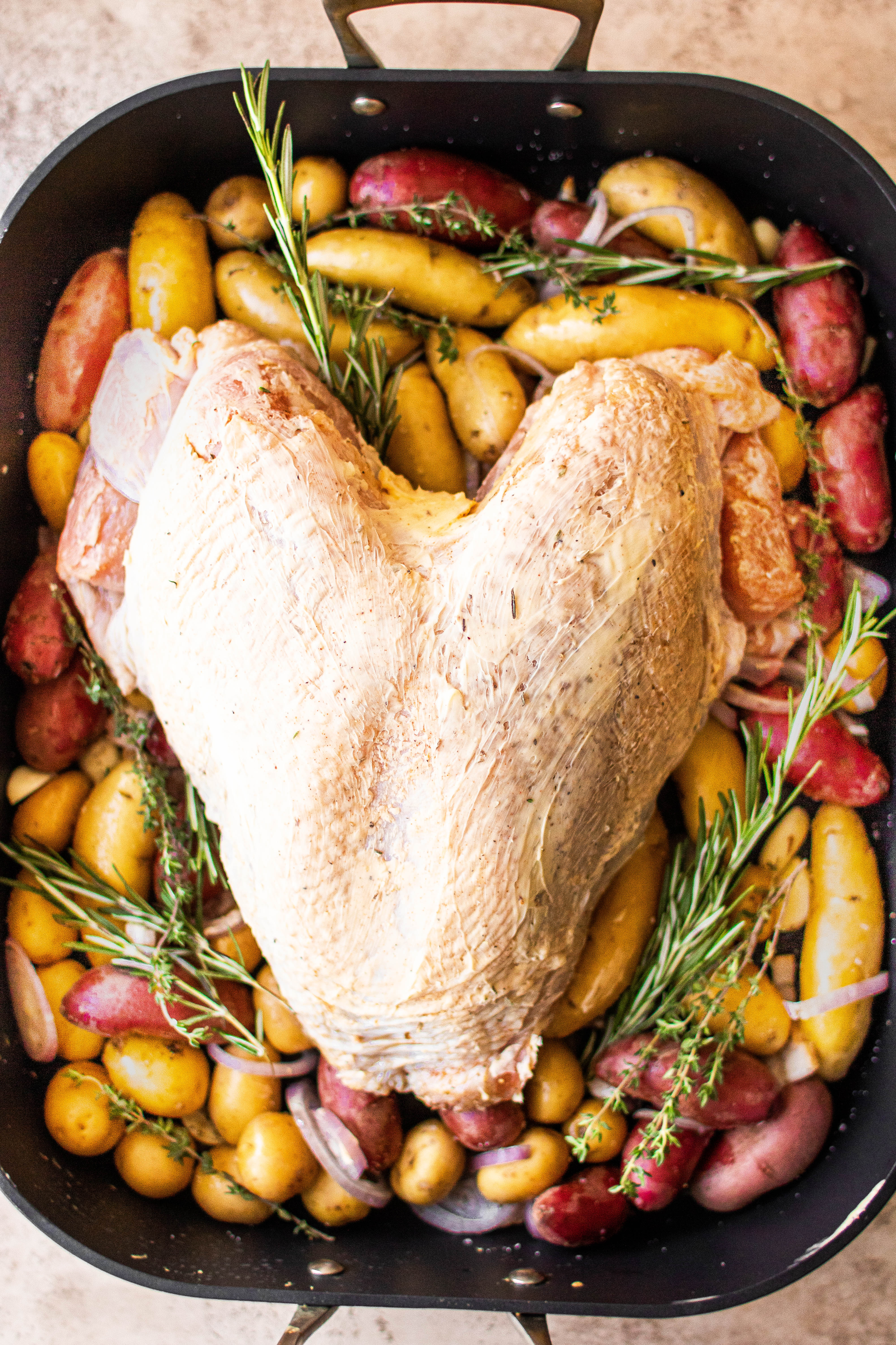 A turkey breast and potatoes, ready for roasting 