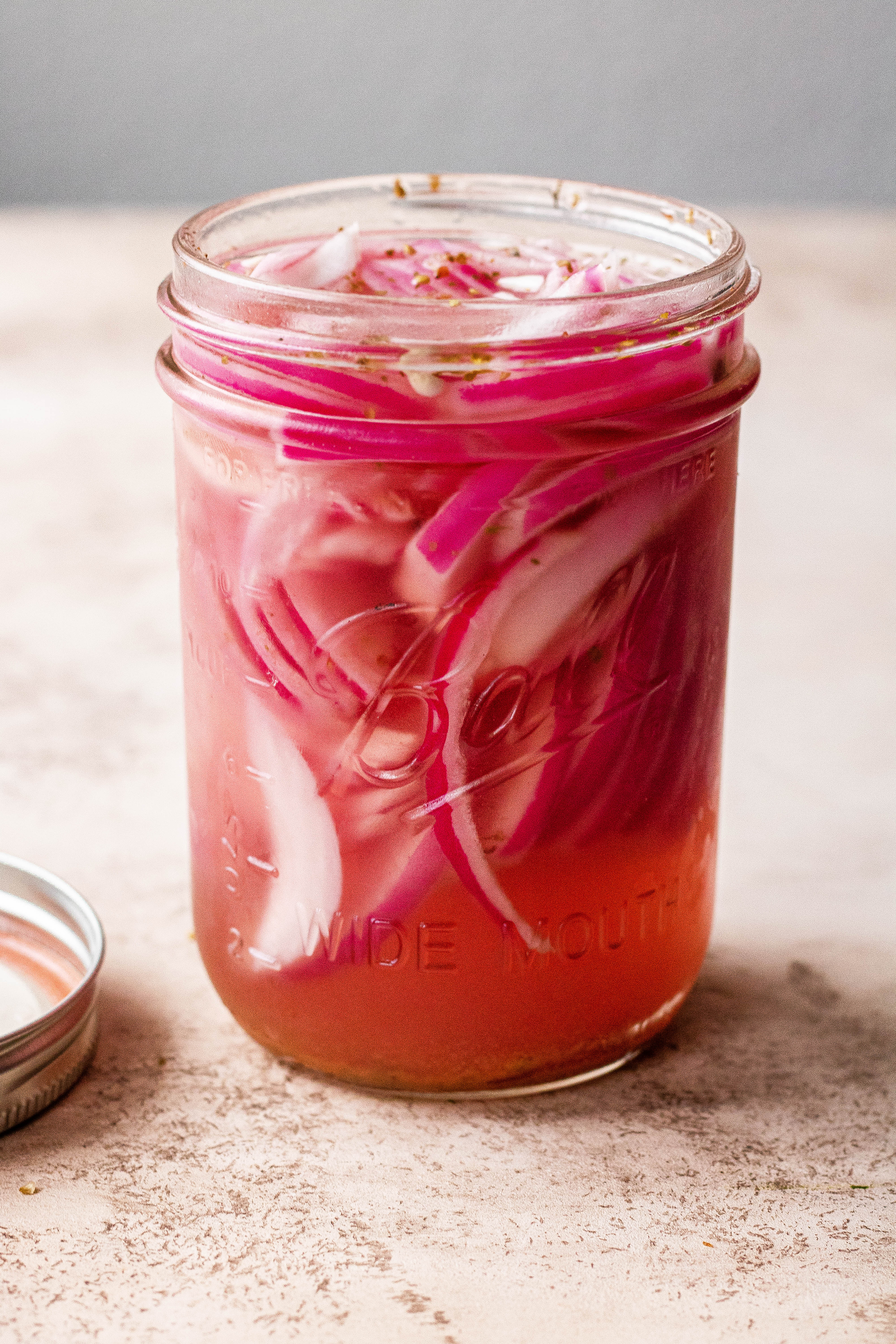 A mason jar full of pickled red onions with the lid off 