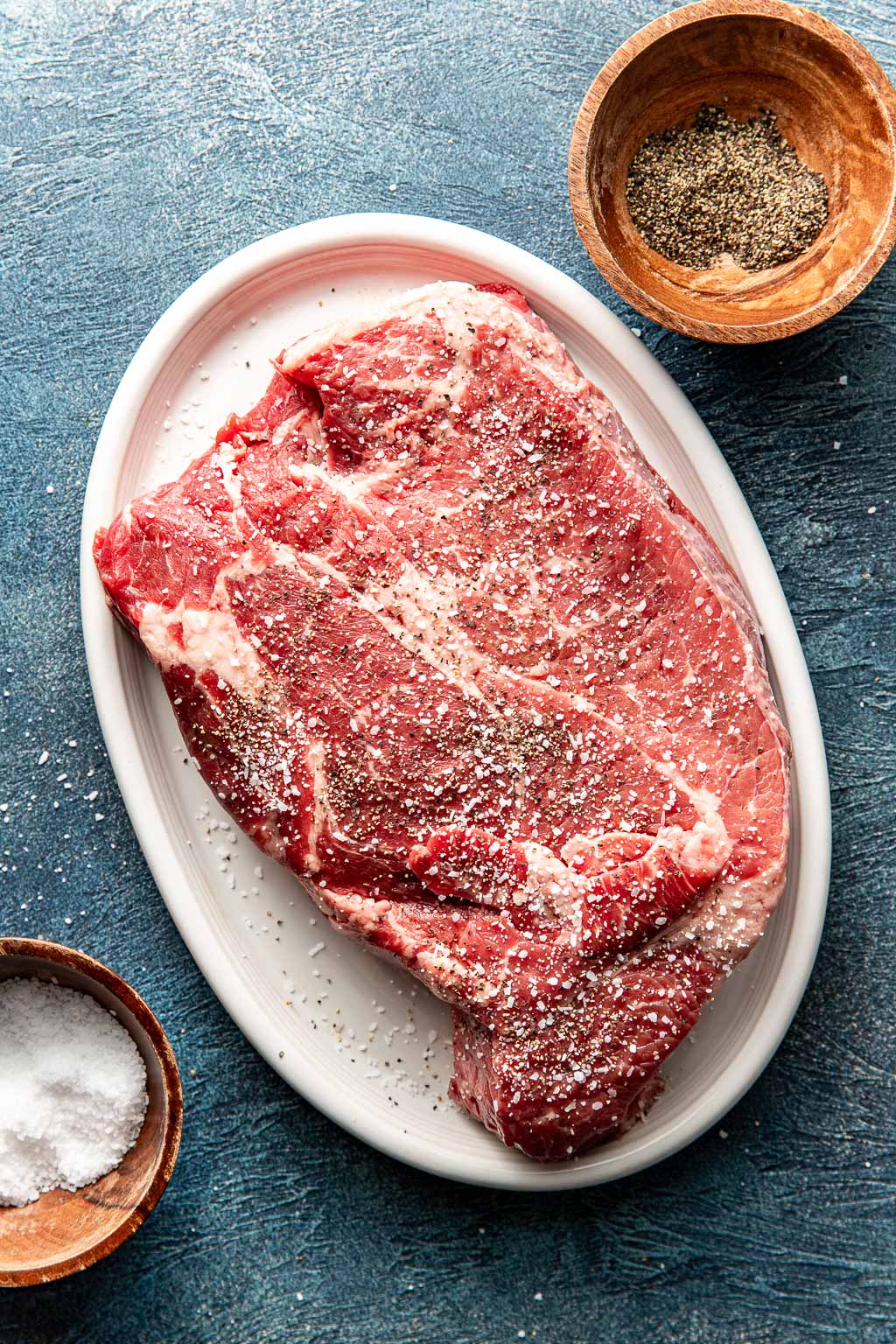 Seasoned chuck roast on a plate before searing