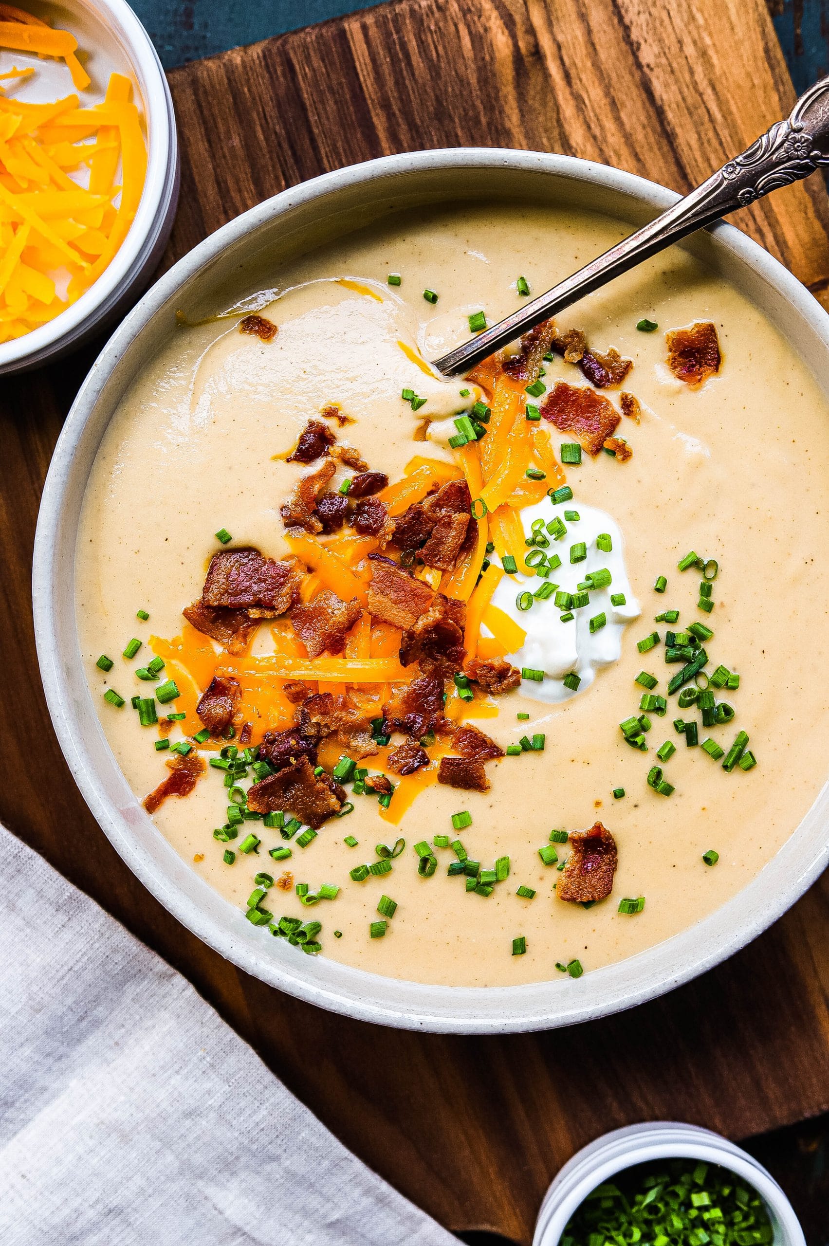 A bowl of loaded cauliflower soup, topped with cheddar, bacon, chives, and sour cream 
