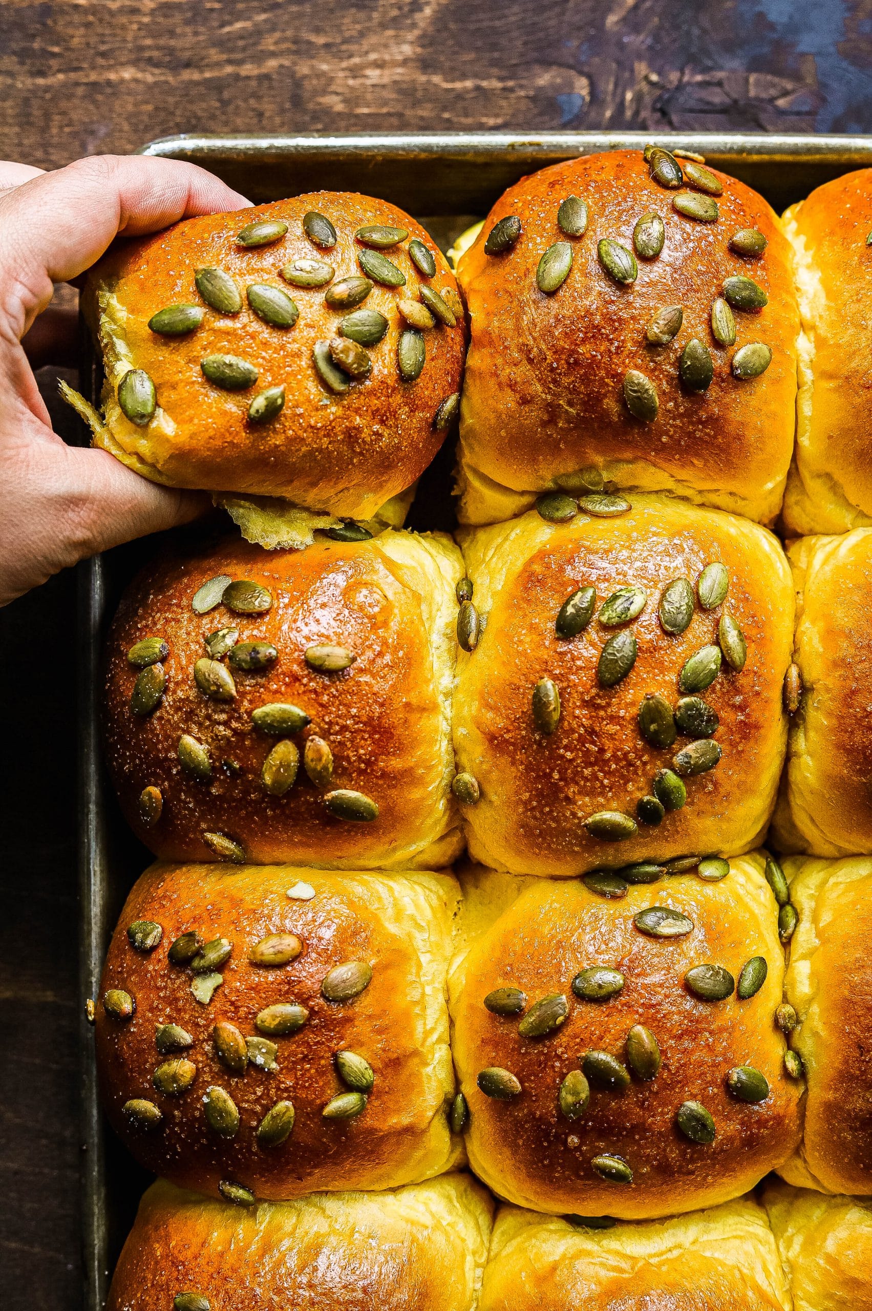 A pumpkin yeast roll being grabbed from a pan of rolls 