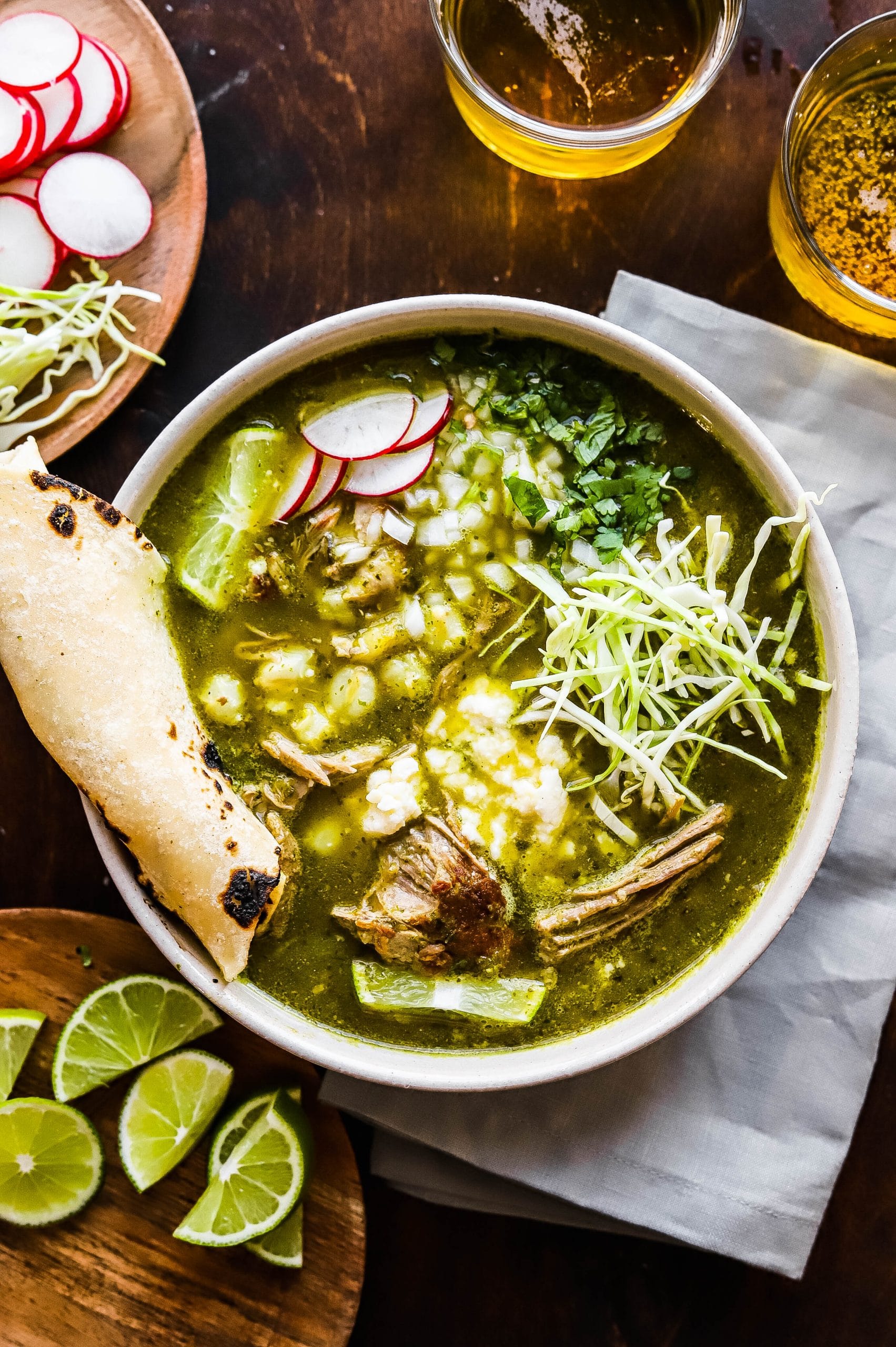 A bowl of pork pozole verde topped with shredded cabbage, onion, radish, and lime. 