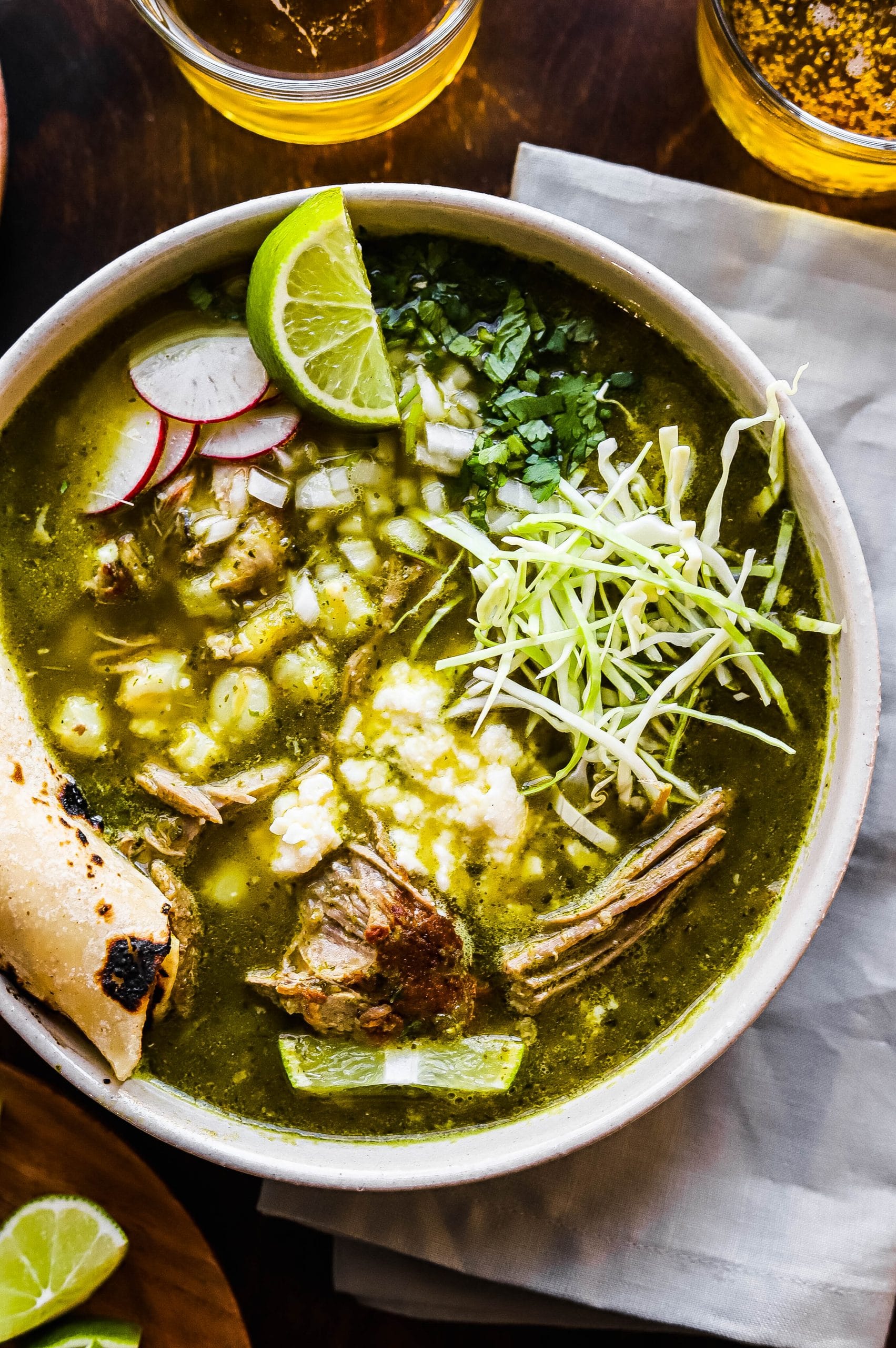 A bowl of pork pozole verde topped with shredded cabbage, onion, radish, and lime. 