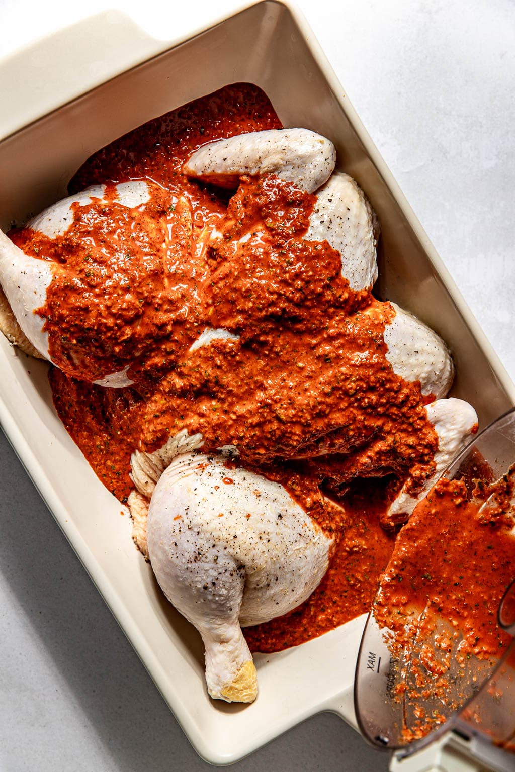 pollo asado marinade being poured over the chicken in a baking dish