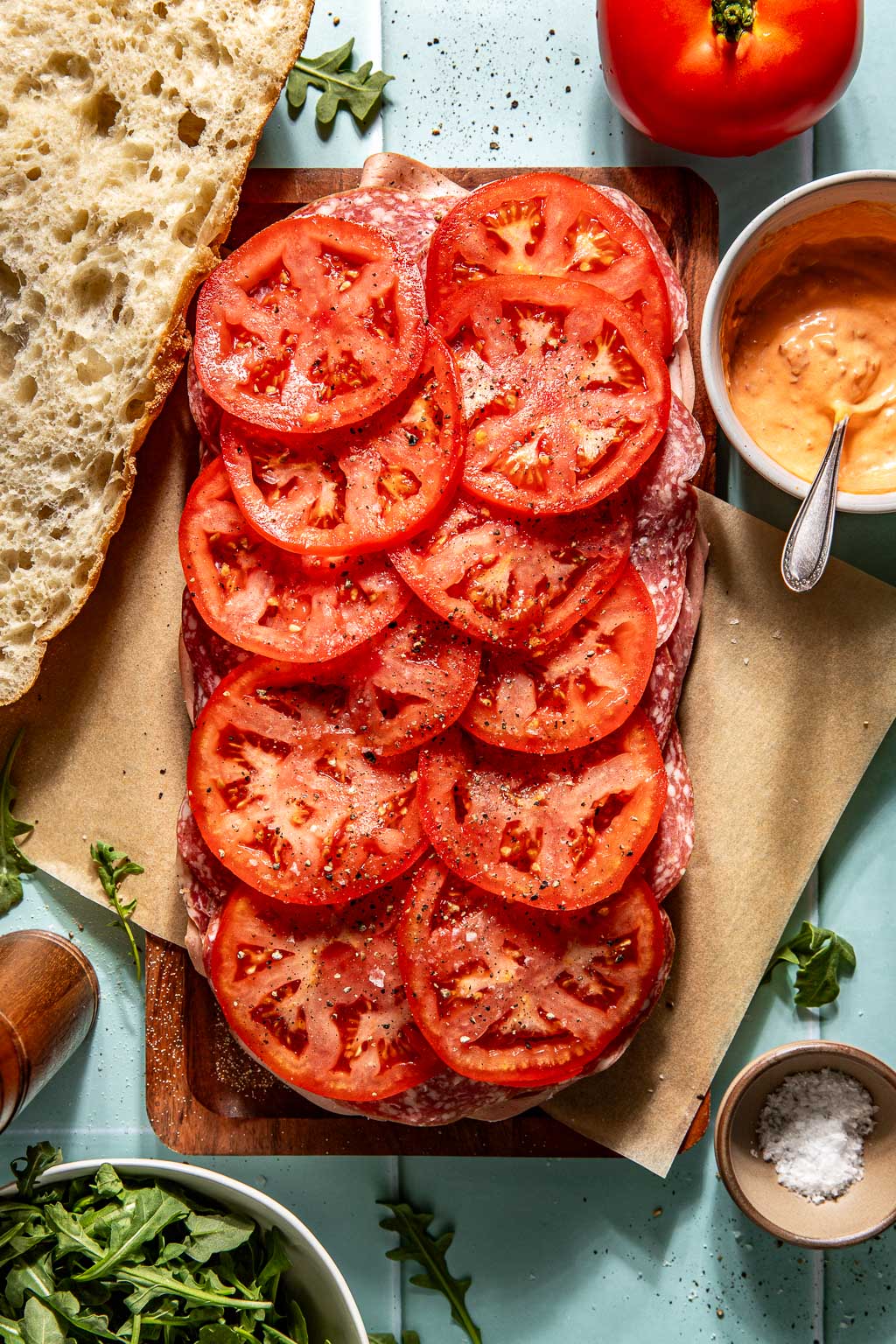 Sliced tomatoes being added to an Italian picnic sandwich