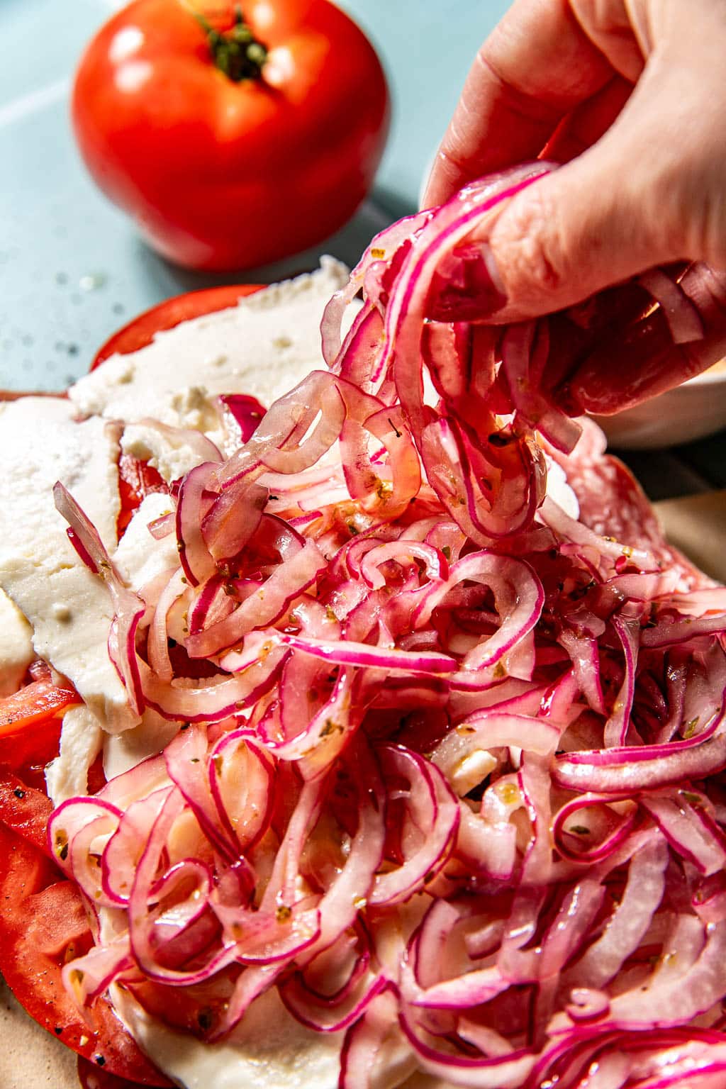 Marinated onions being added to an Italian picnic sandwich