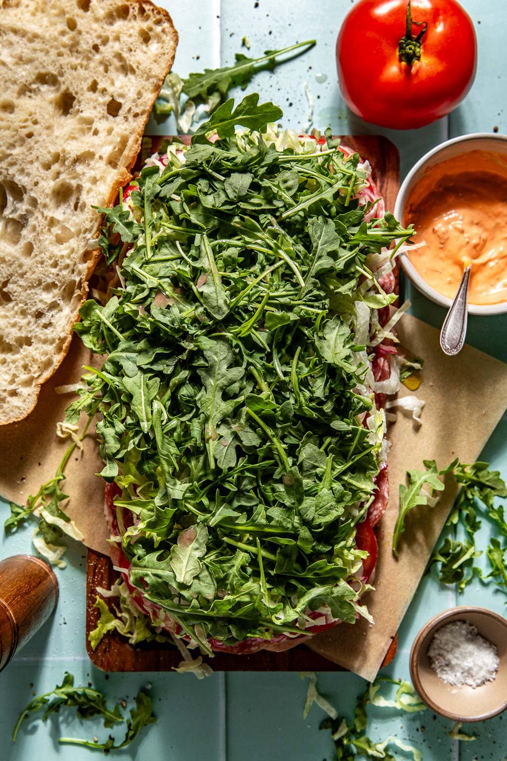 Arugula being added to an Italian picnic sandwich