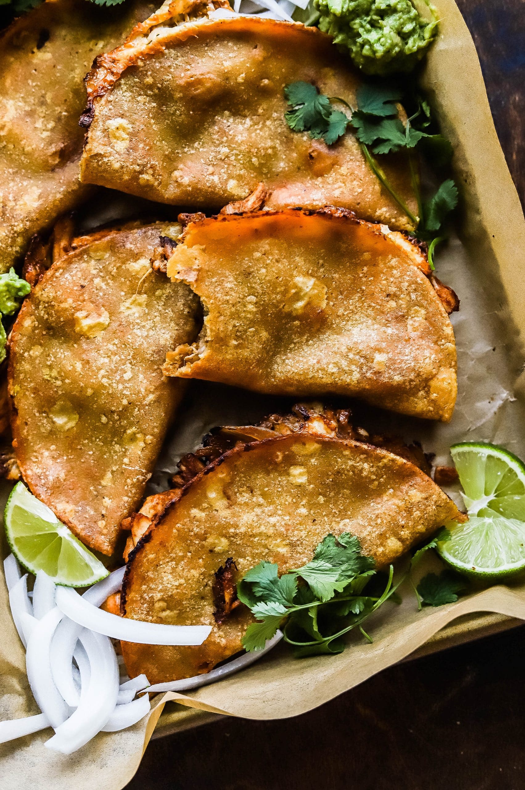 baked chicken tacos piled on a sheet pan; one has a bite missing 