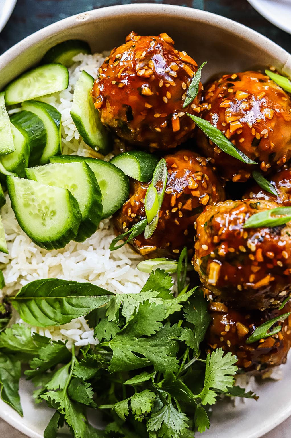 Sticky Asian-style meatballs over rice, with cucumbers and herbs 