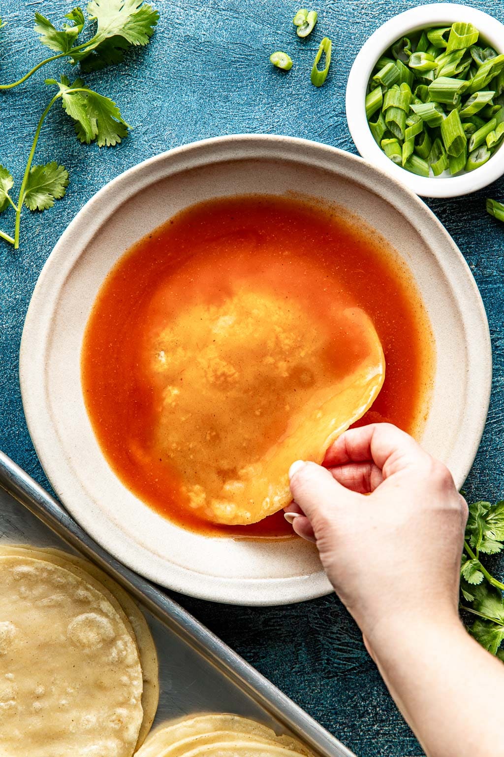 corn tortilla being dipping in enchilada sauce
