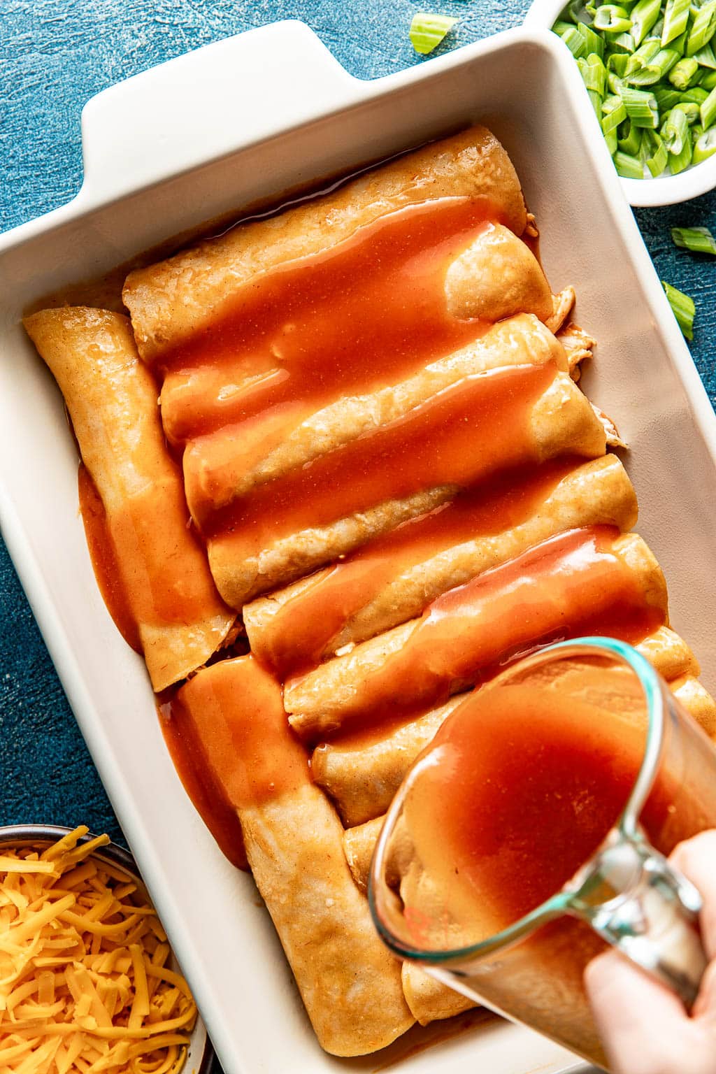 enchilada sauce being poured over rolled enchiladas