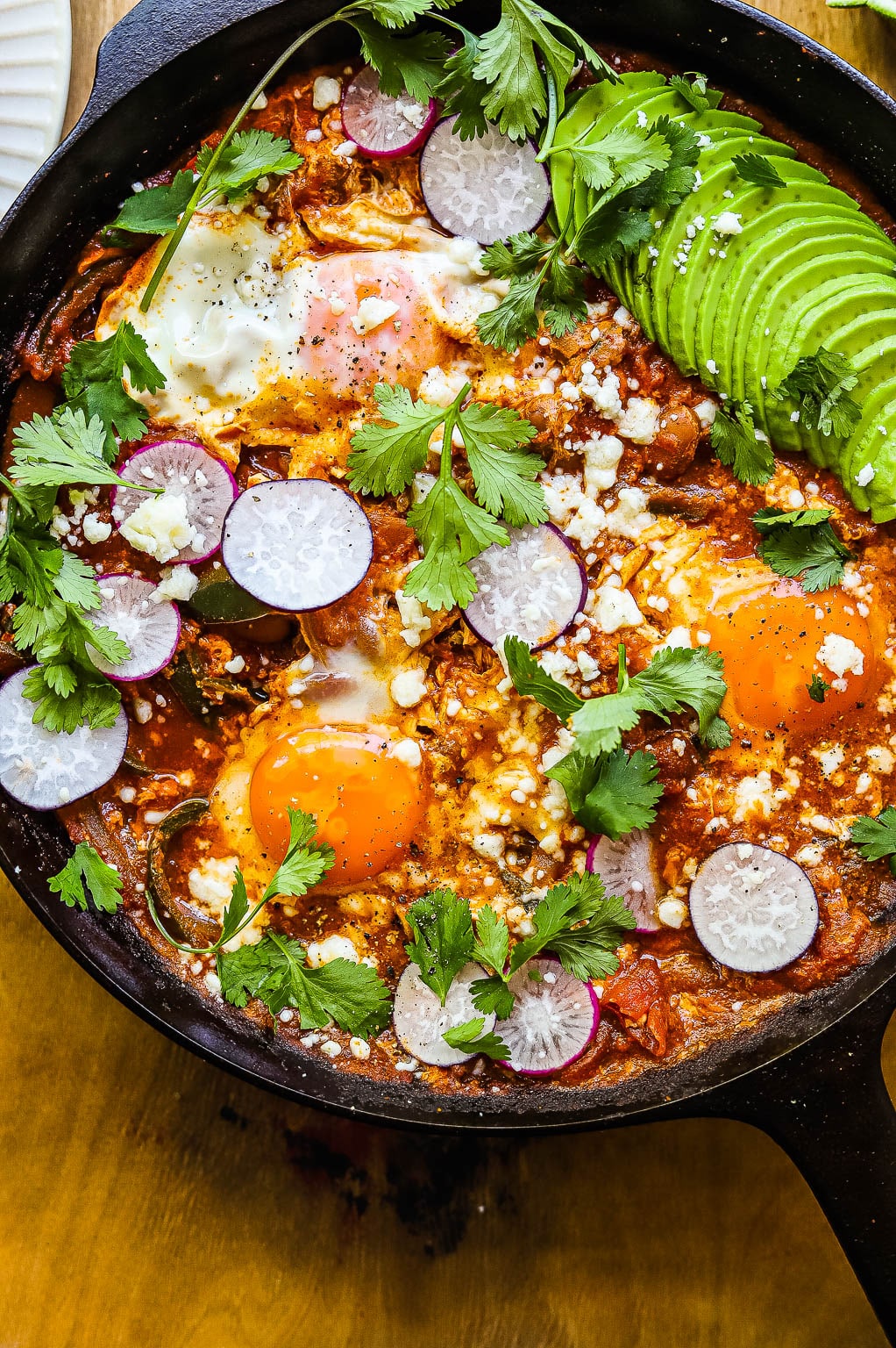 huevos rancheros in a skillet topped with avocado and sliced radish 