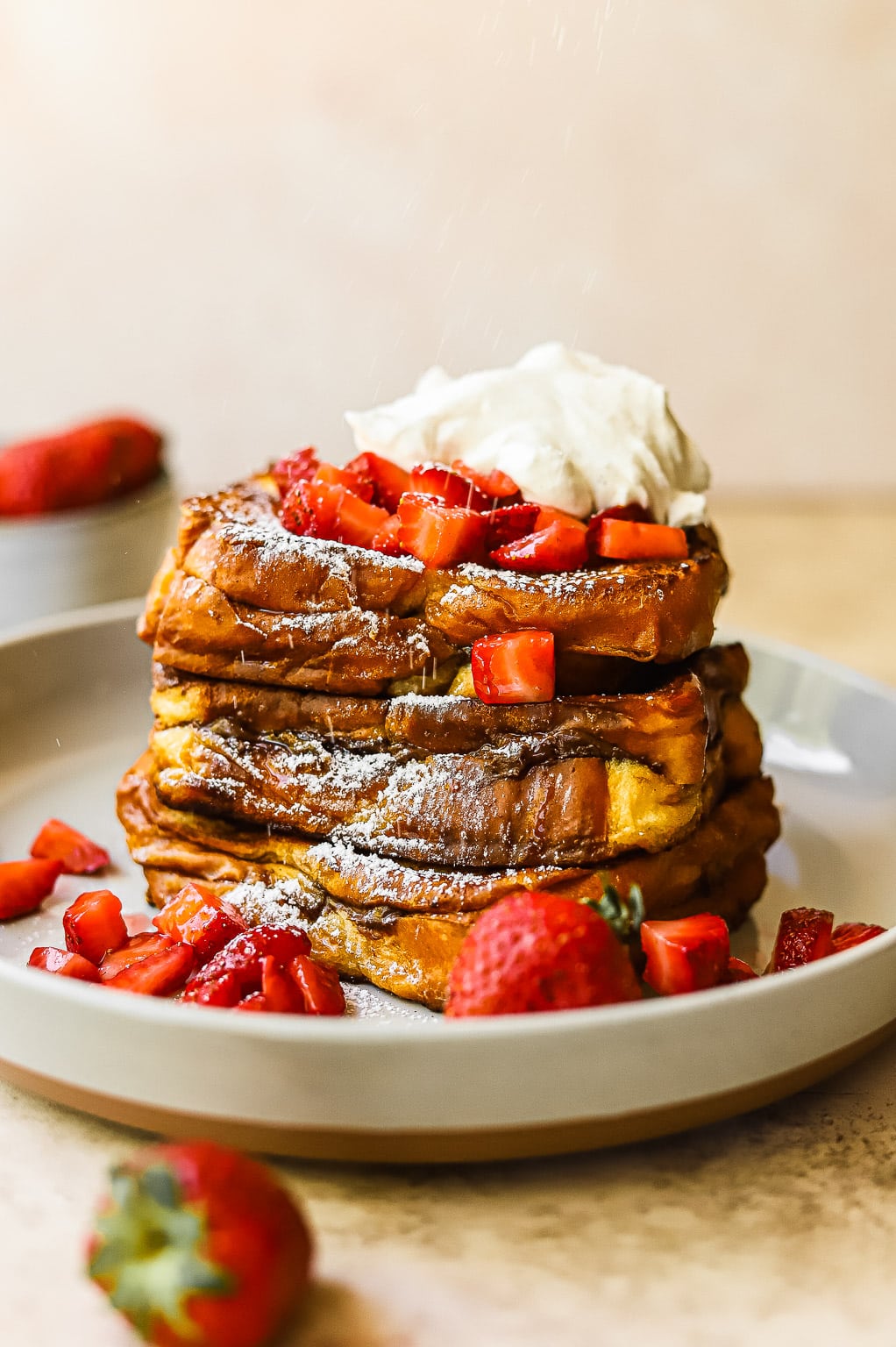 A stack of Nutella stuffed french toast topped with macerated strawberries and whipped cream
