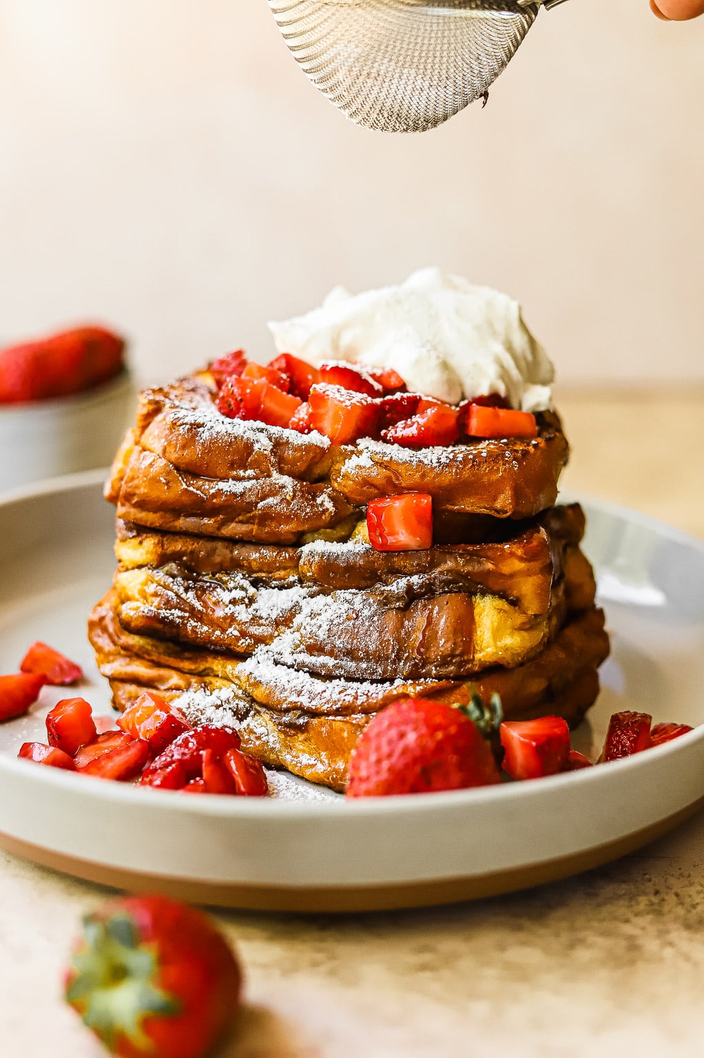 A stack of Nutella stuffed french toast topped with macerated strawberries and whipped cream