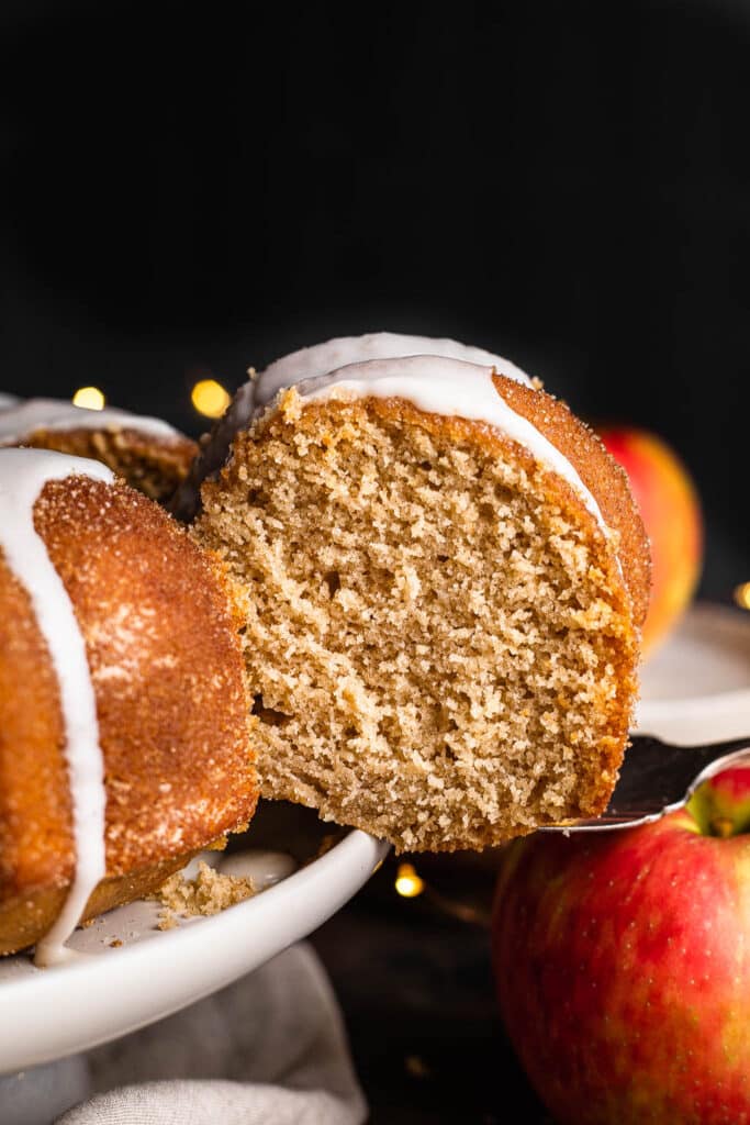 A slice of apple cider donut cake being taken from cake stand 