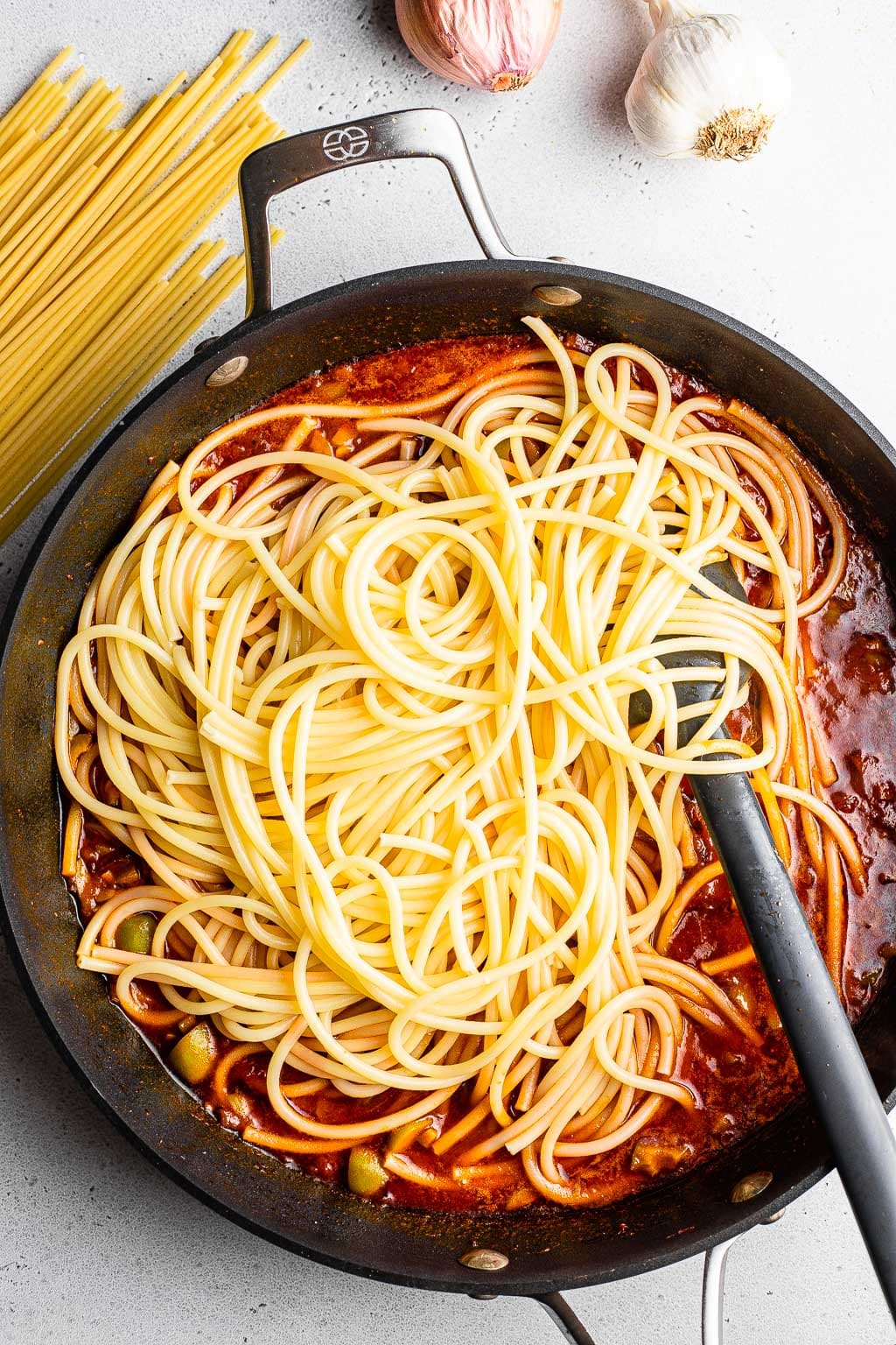 Bucatini noodles in a pan of shallot pasta sauce. 