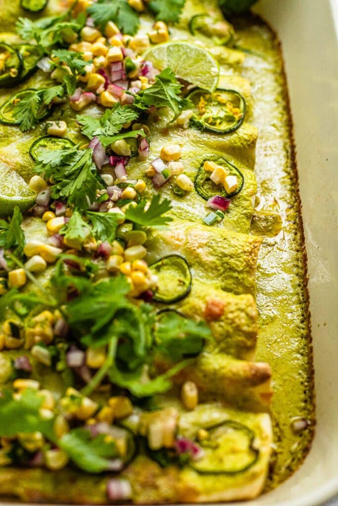 Ground beef enchiladas with green sauce, topped with corn, cilantro, lime, and onion 