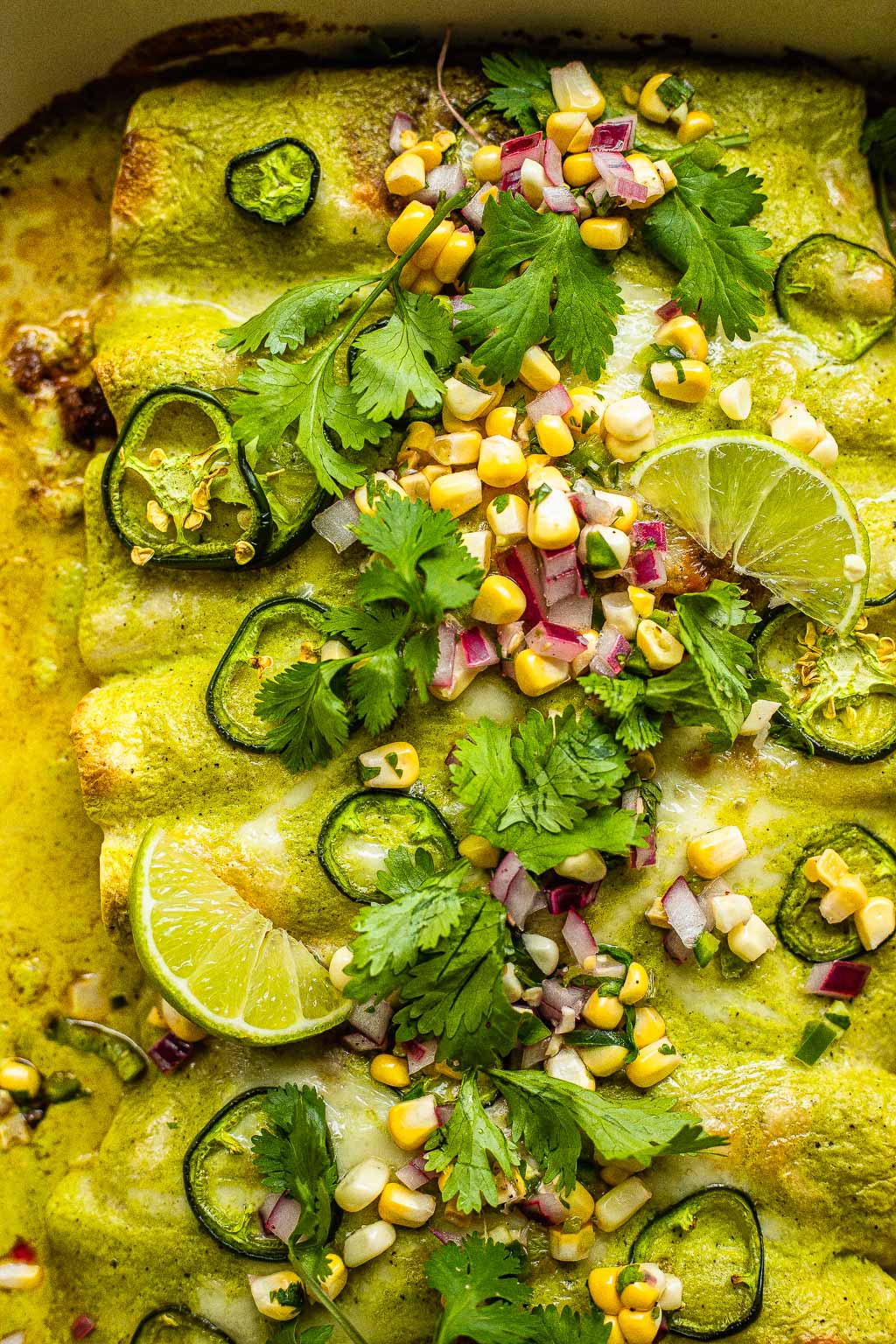 Ground beef enchiladas with green sauce, topped with corn, cilantro, lime, and onion 