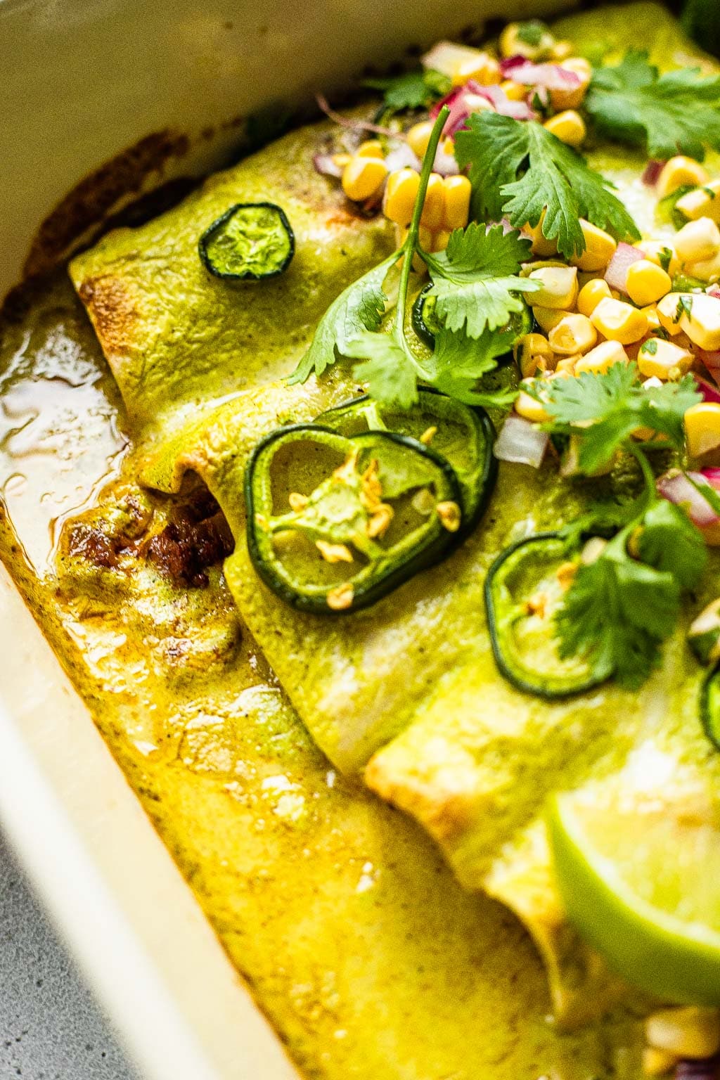 Close up of ground beef enchiladas with green sauce, loaded with toppings 