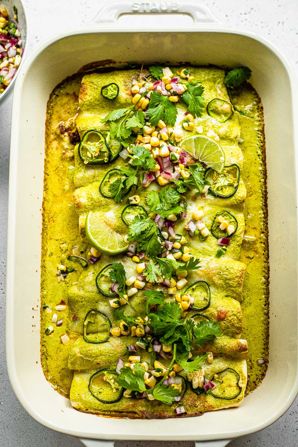Green beef enchiladas topped with corn, cilantro, lime, and onion 