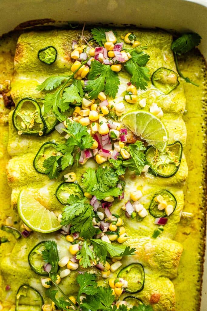 Ground beef enchiladas with green sauce, topped with corn, cilantro, lime, and onion 