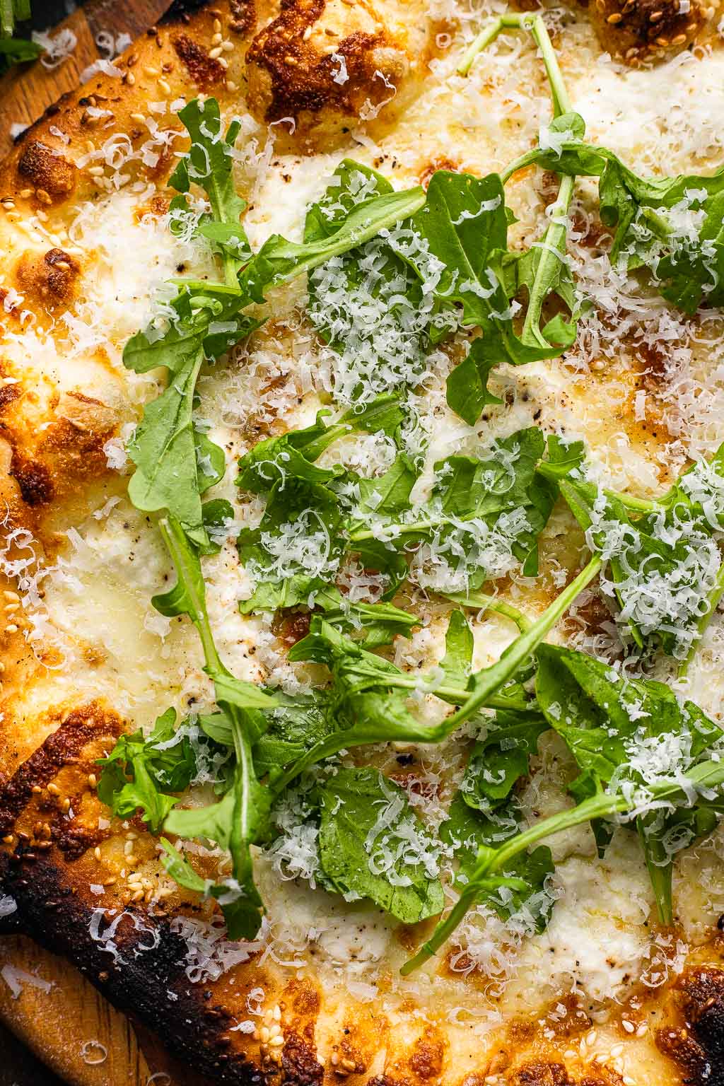 Overhead view of a pizza bianca topped with Parmesan and arugula. 