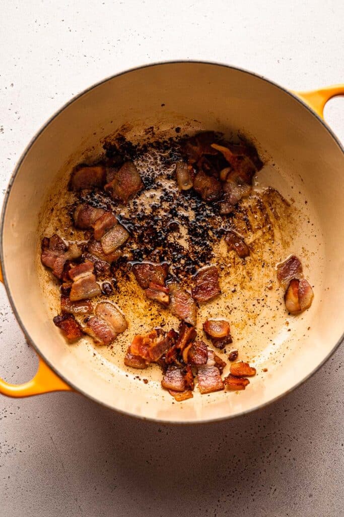 A process shot showing bacon being cooked in a dutch oven. 