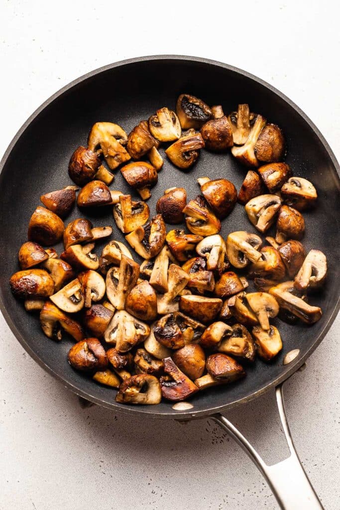 A process shot showing mushrooms browning in a skillet. 