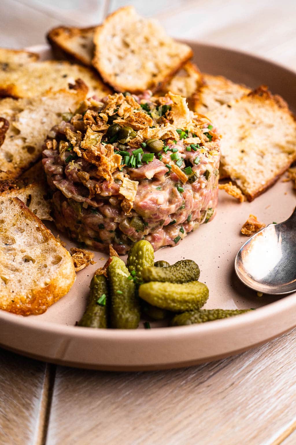 Steak tartare on a plate with bread and cornichons
