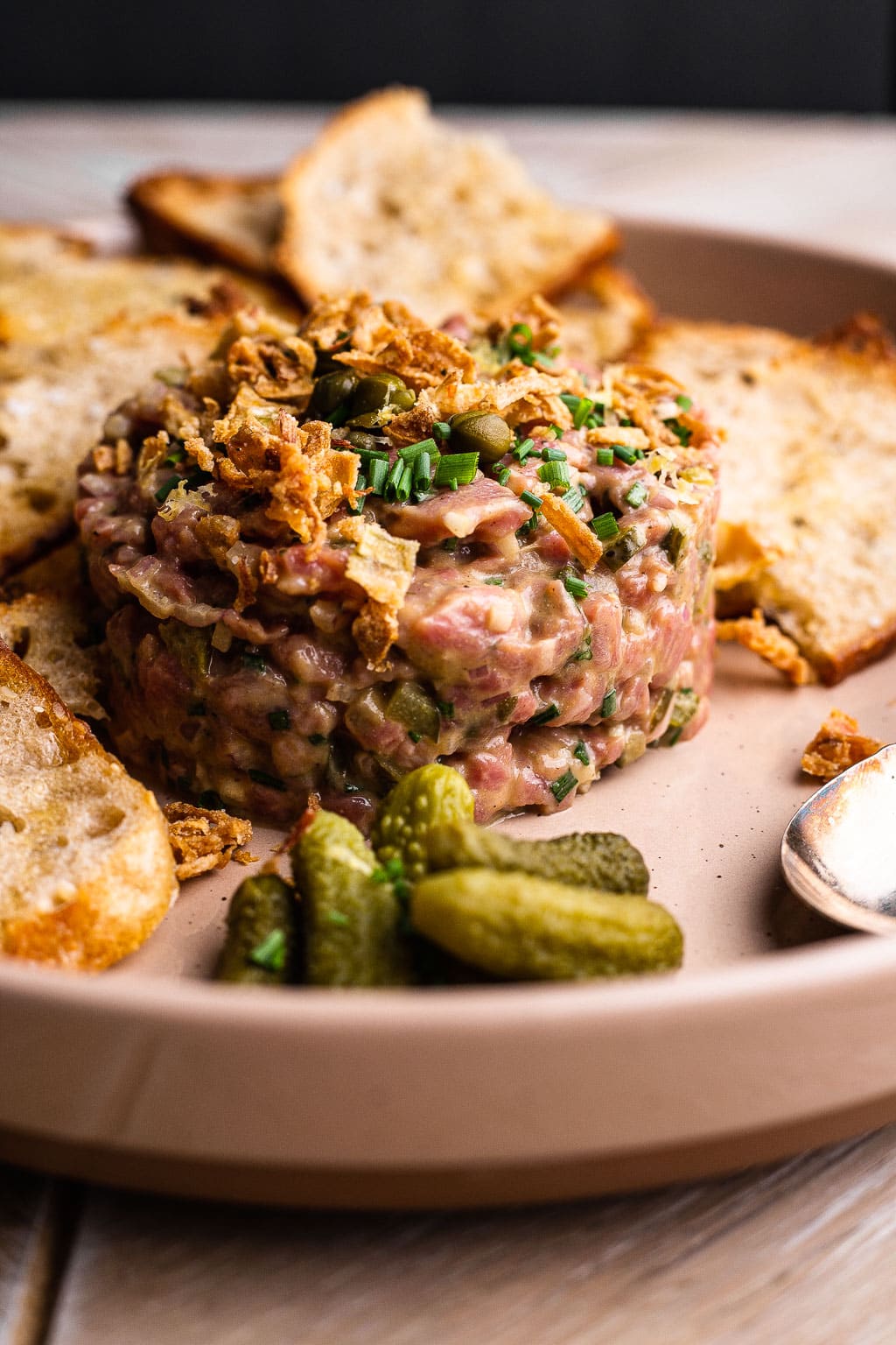 Steak tartare on a plate with bread and cornichons