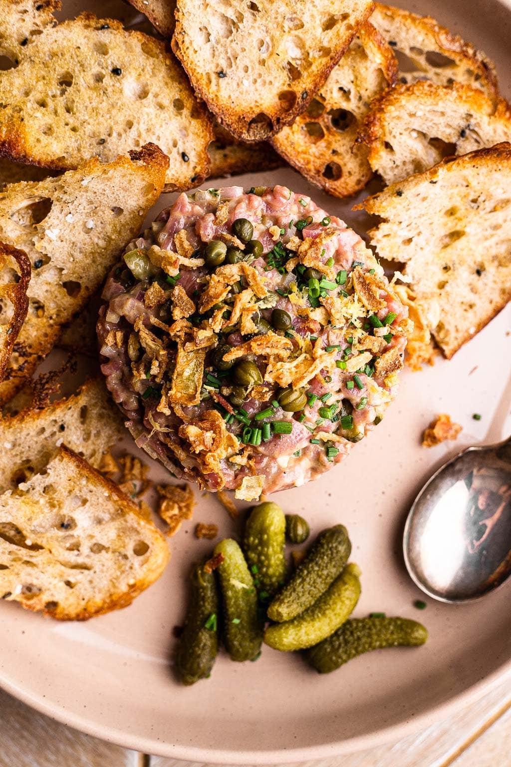Steak tartare on a plate with bread and cornichons