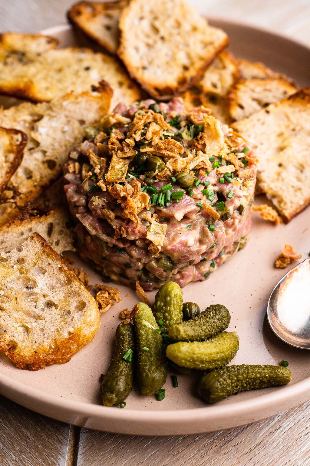 Steak tartare on a plate with bread and cornichons