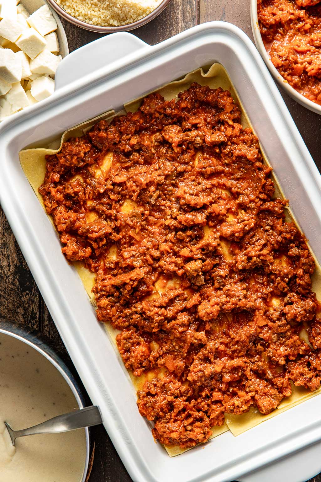 Spreading bolognese sauce over lasagna noodles. 