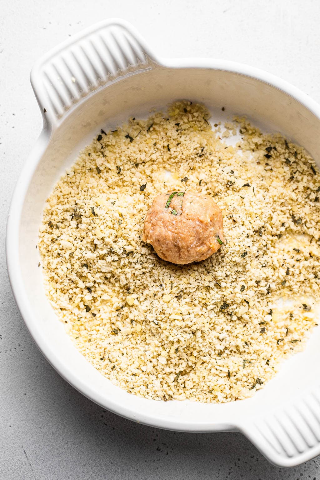 A meatball being rolled in panko