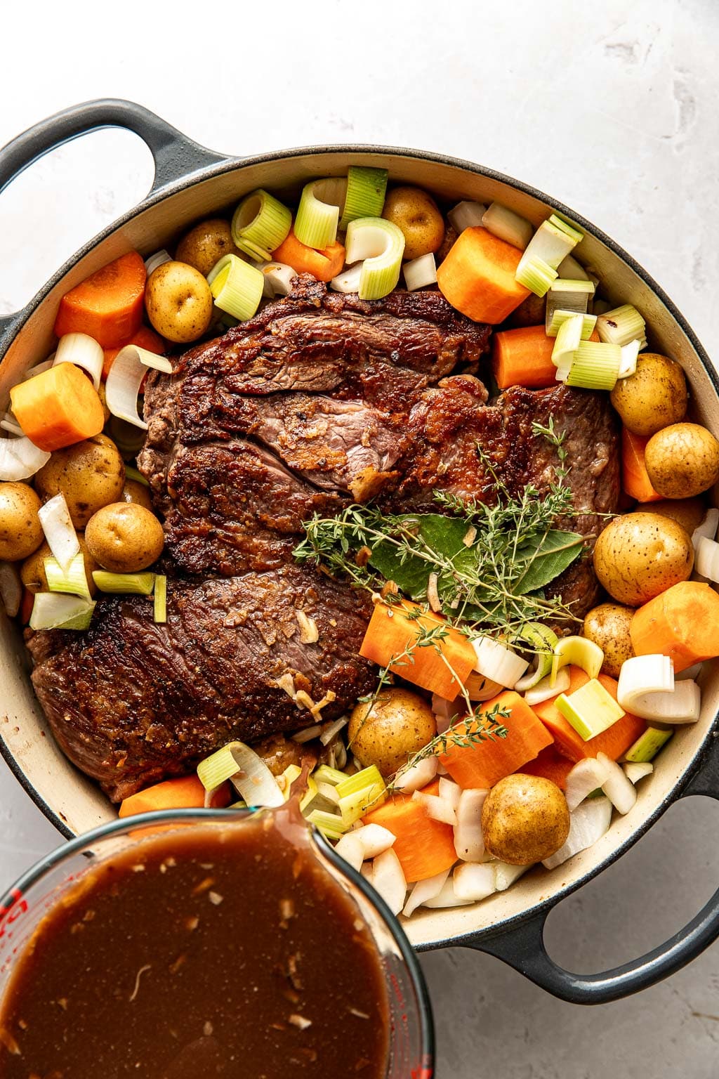 braising liquid being poured over the pot roast in a dutch oven